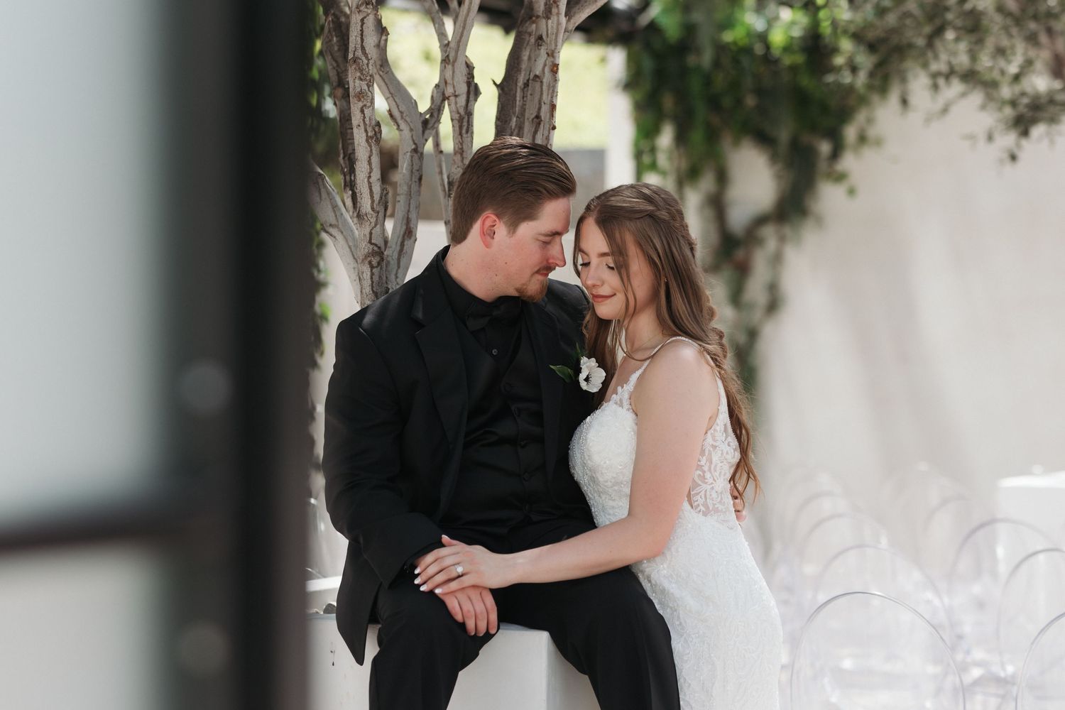Tender moment between newlyweds against white wall with climbing vines.