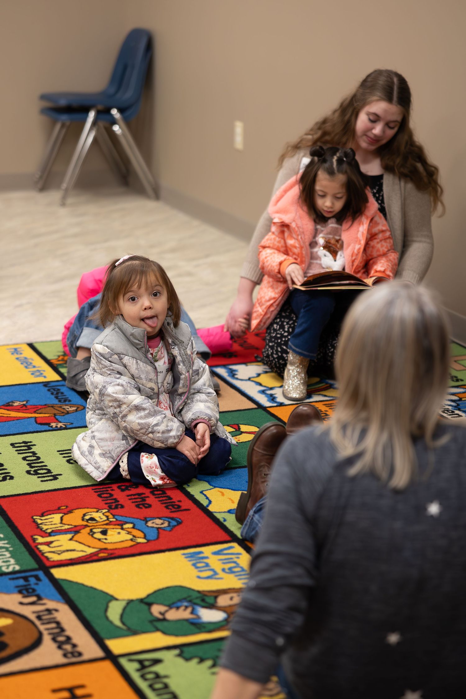 Group sitting on educational alphabet carpet during indoor learning activity.