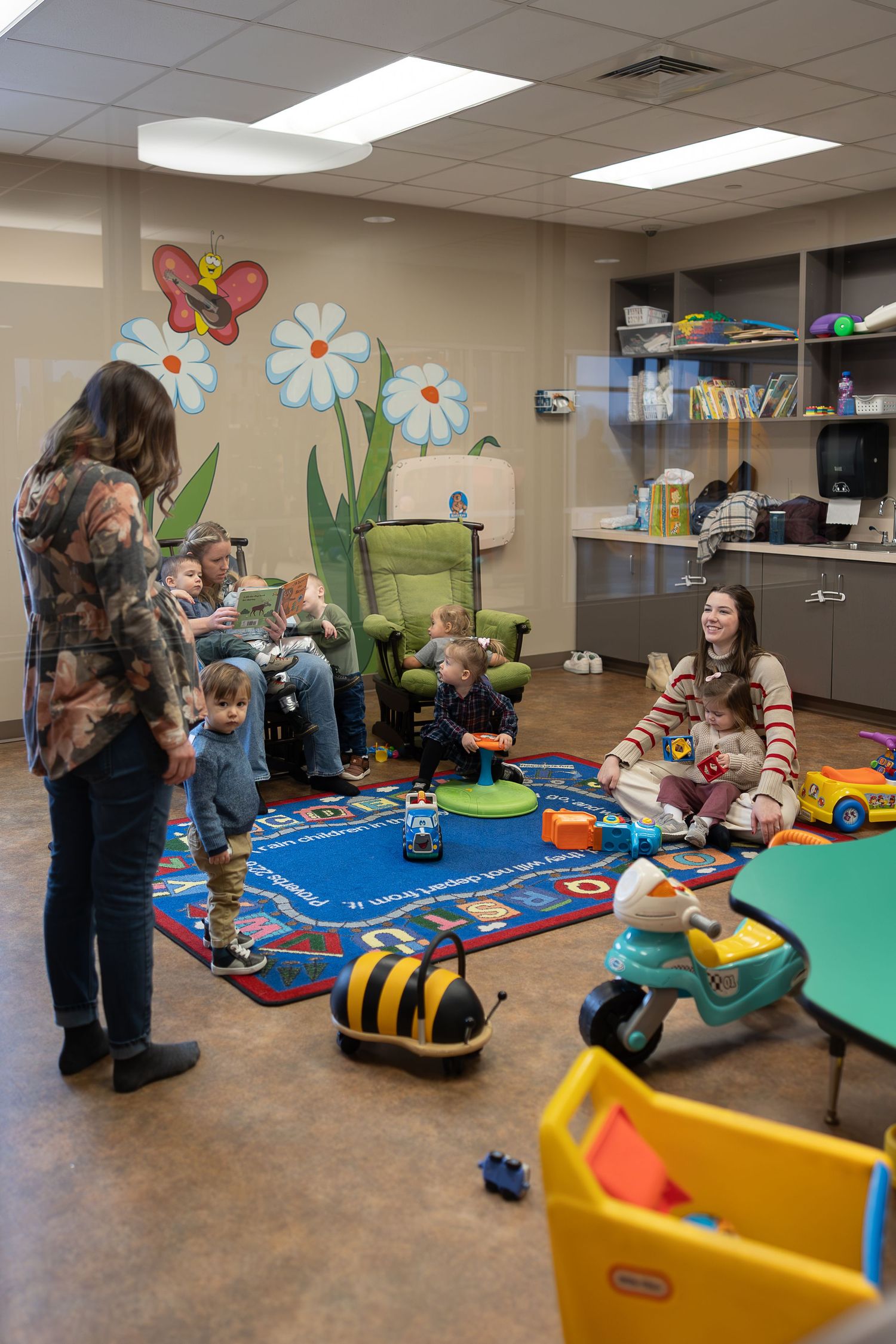 Daycare room with painted flower mural and children playing on blue carpet.