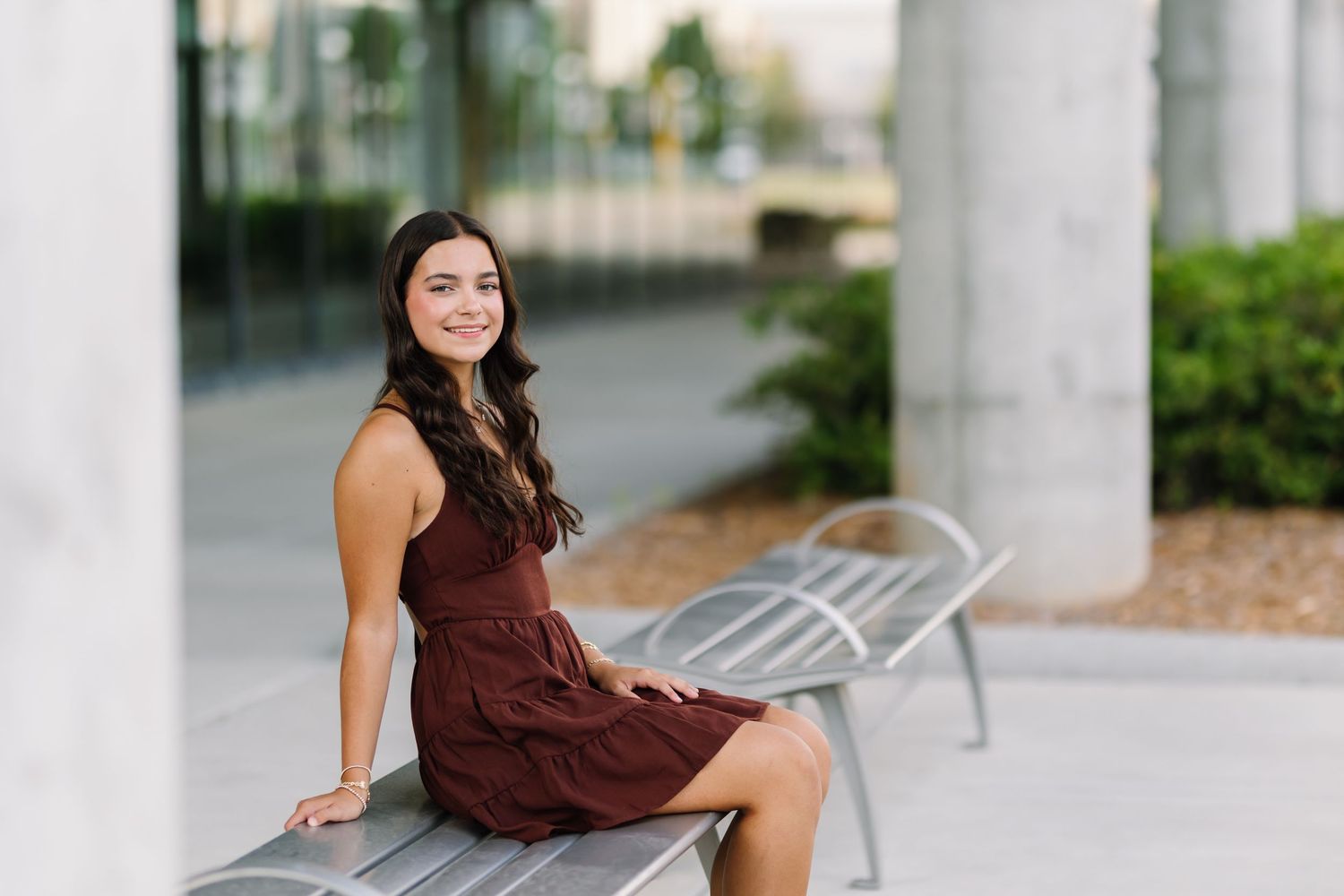 A woman in a burgundy dress poses elegantly in front of white architectural columns.
