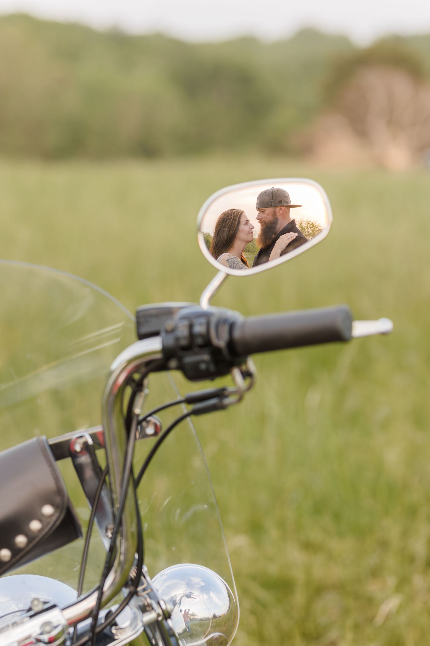 Vintage bicycle handlebars and controls with chrome mirror and leather grips against a soft blurred green background.