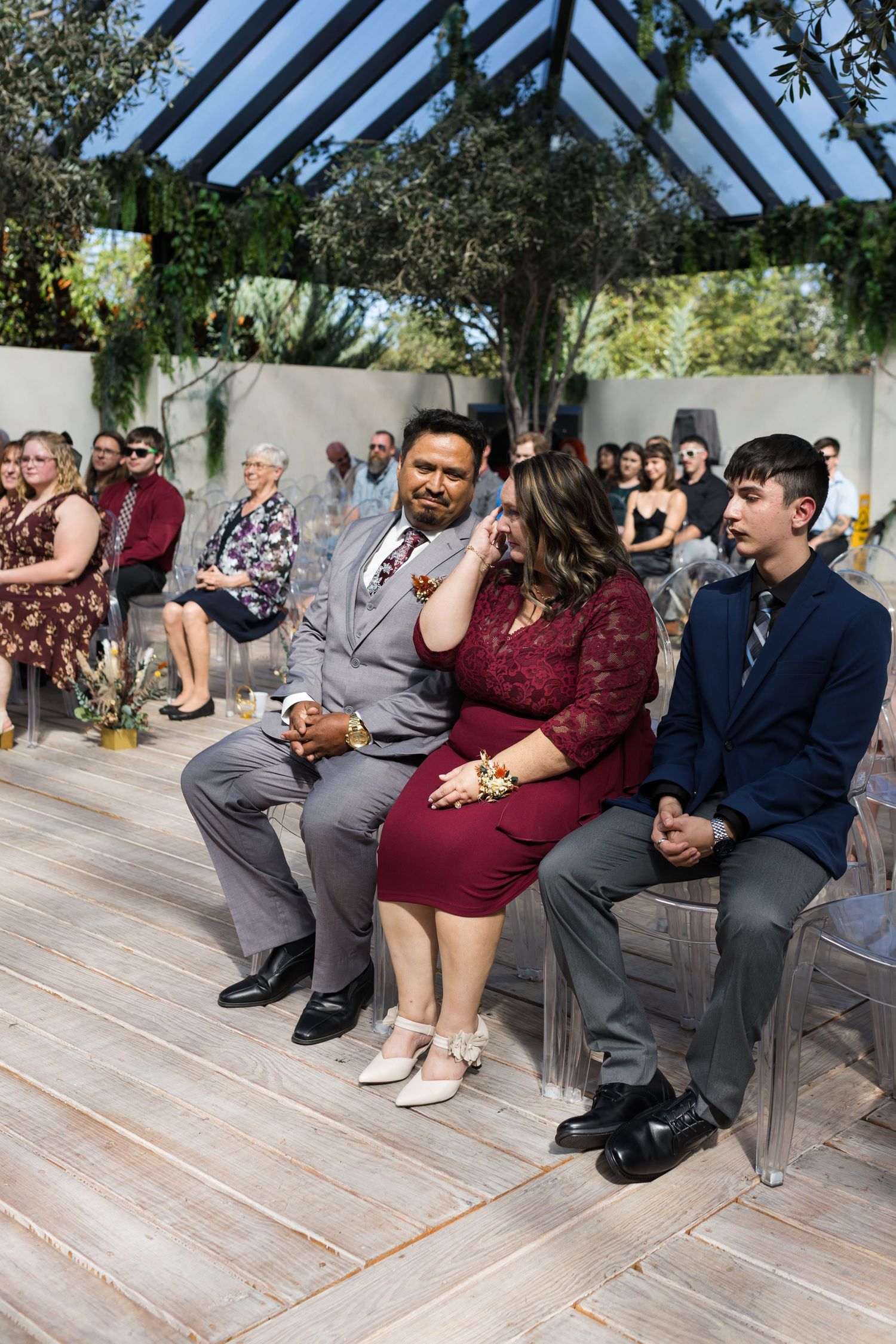 Wedding guests seated in outdoor ceremony, emotional woman in burgundy dress wiping tears of joy.