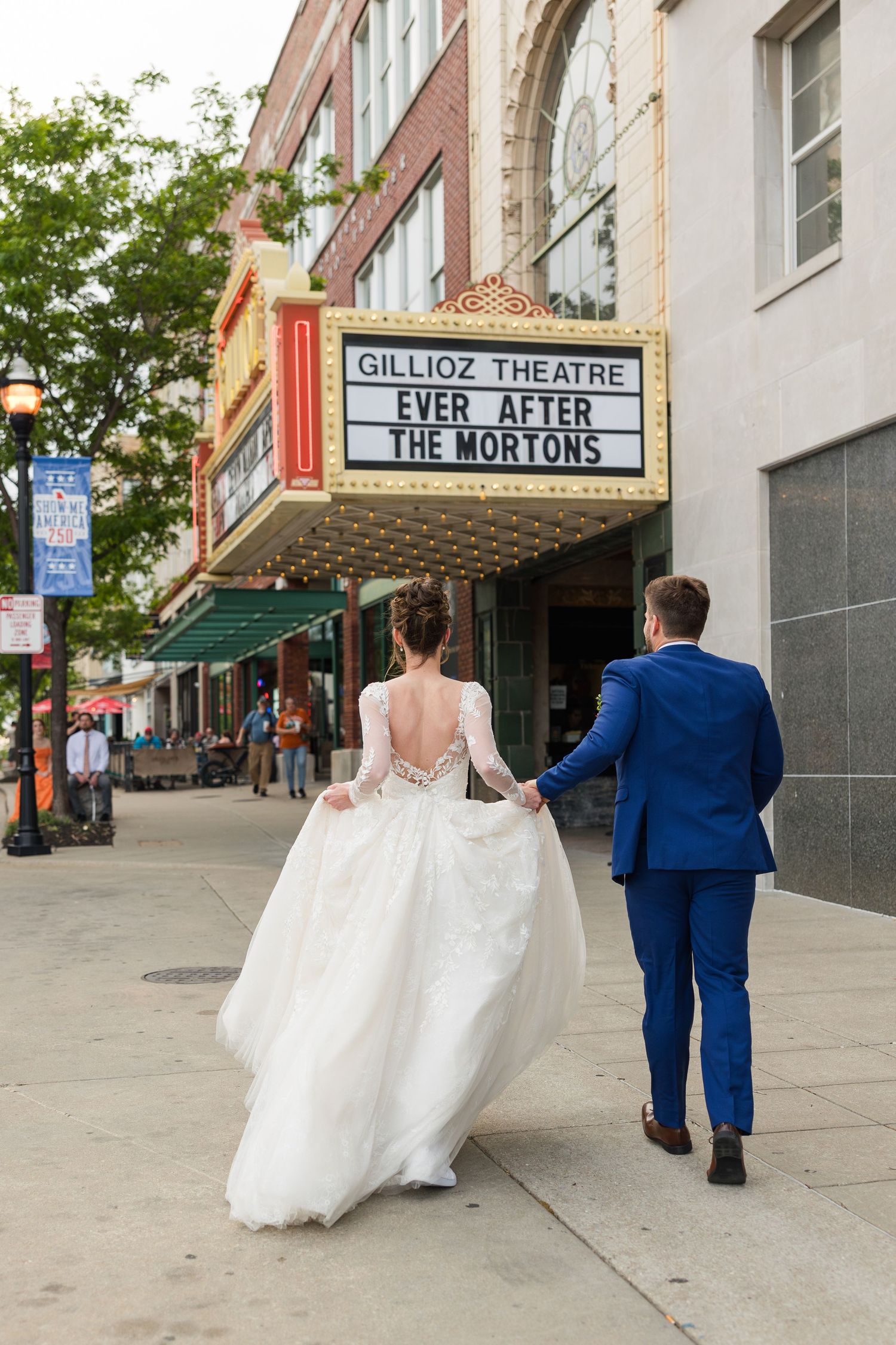 Bride and groom walk hand in hand toward Gillioz Theatre marquee reading Ever After The Mortons.