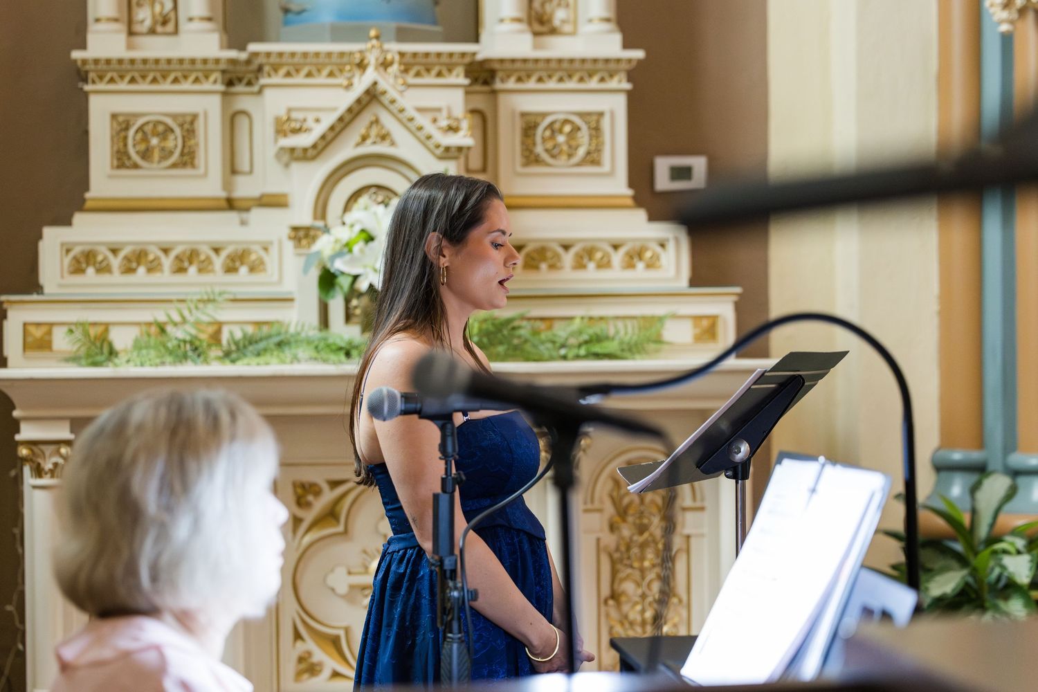 Elegant woman in blue off-shoulder gown performs at a church altar podium during a wedding ceremony.