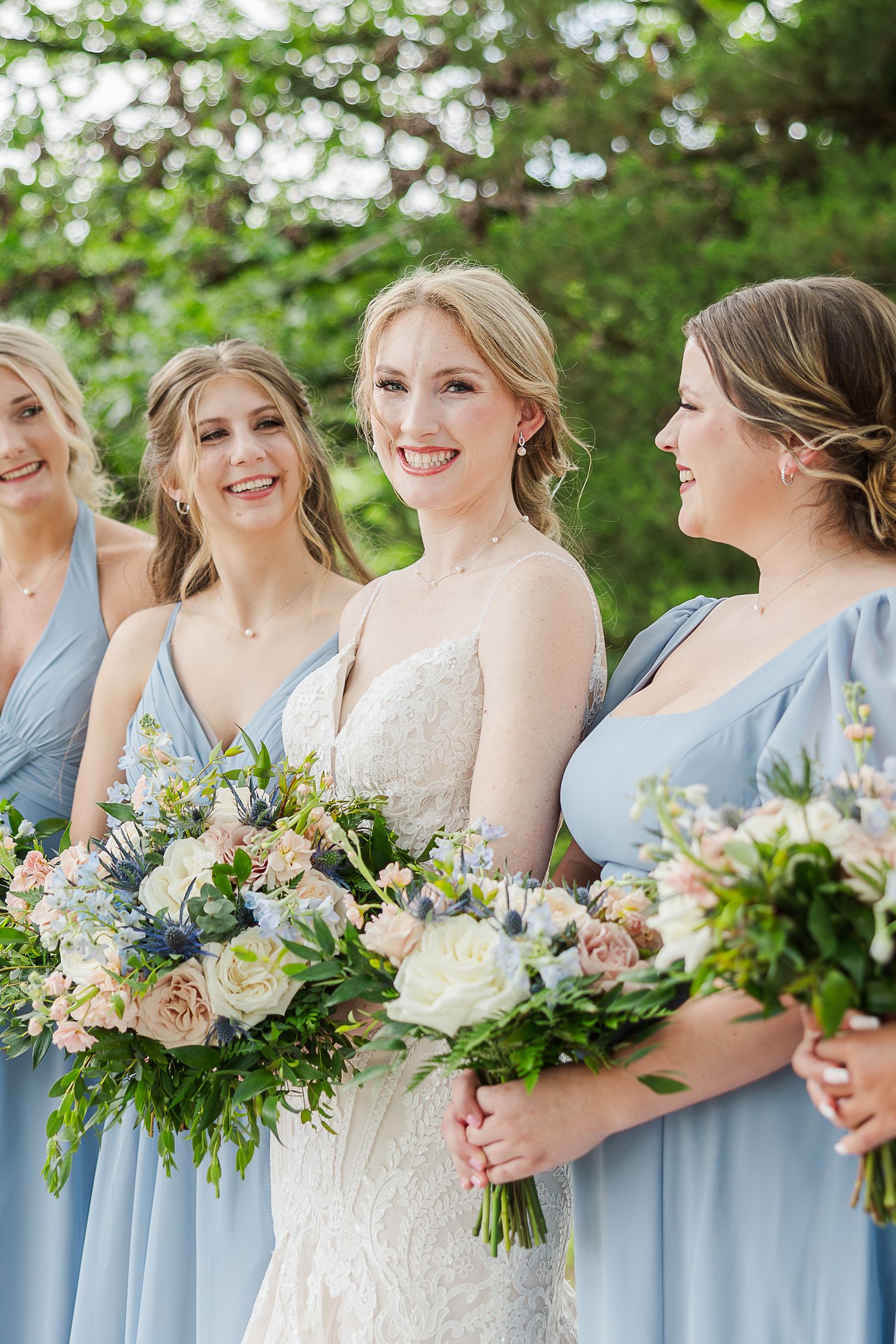 Wedding party wearing light blue bridesmaid dresses holding lush bouquets with pink and white flowers and greenery.