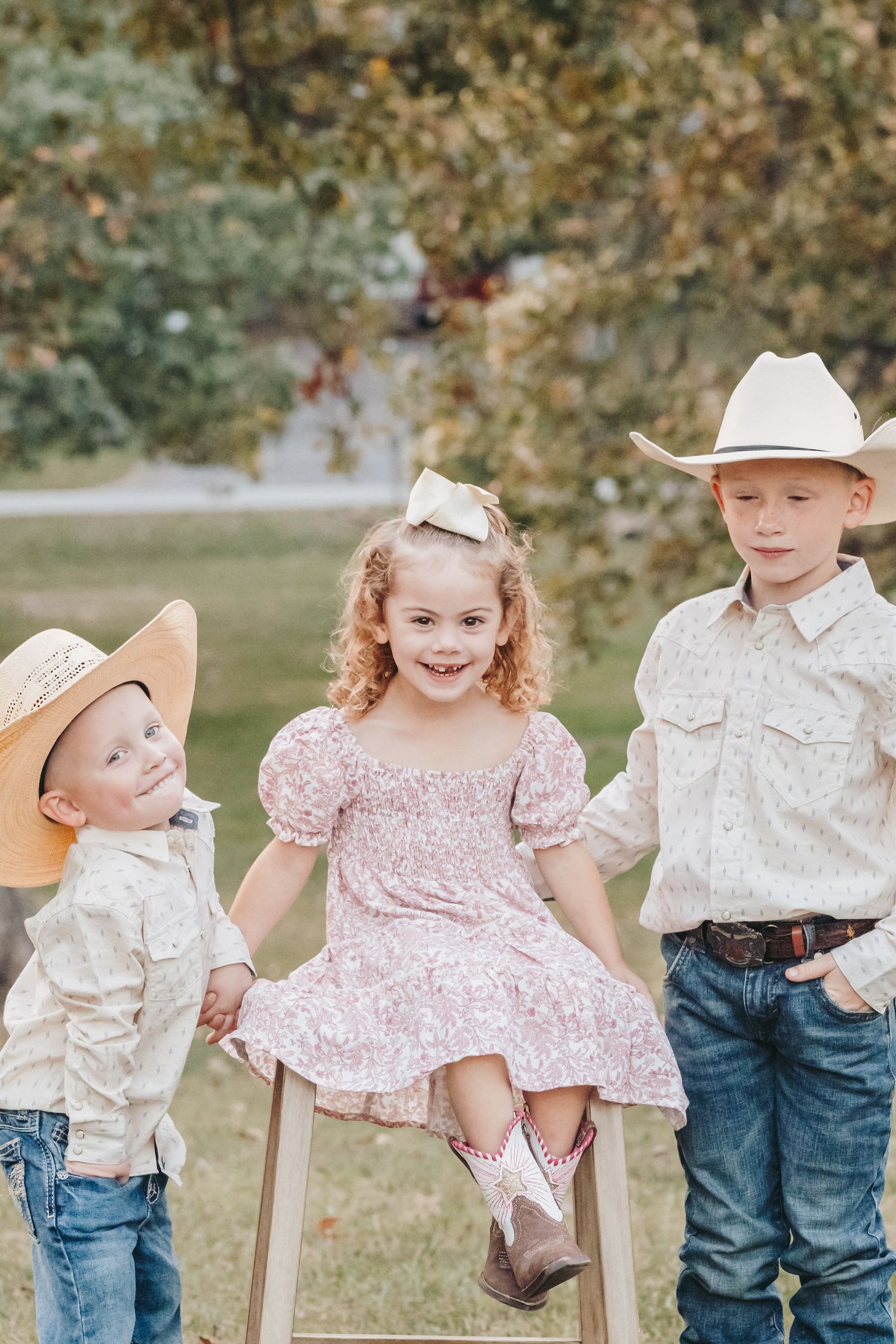 Children in country attire playfully pose with a wooden step stool outdoors.