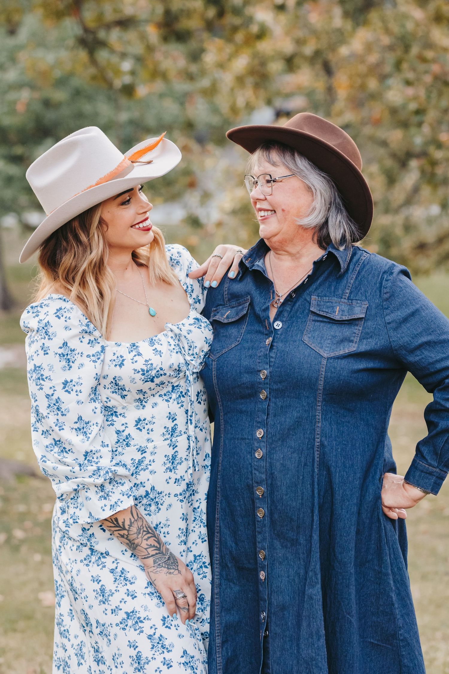 Two people in western attire share a laugh together outdoors wearing denim and floral dresses.