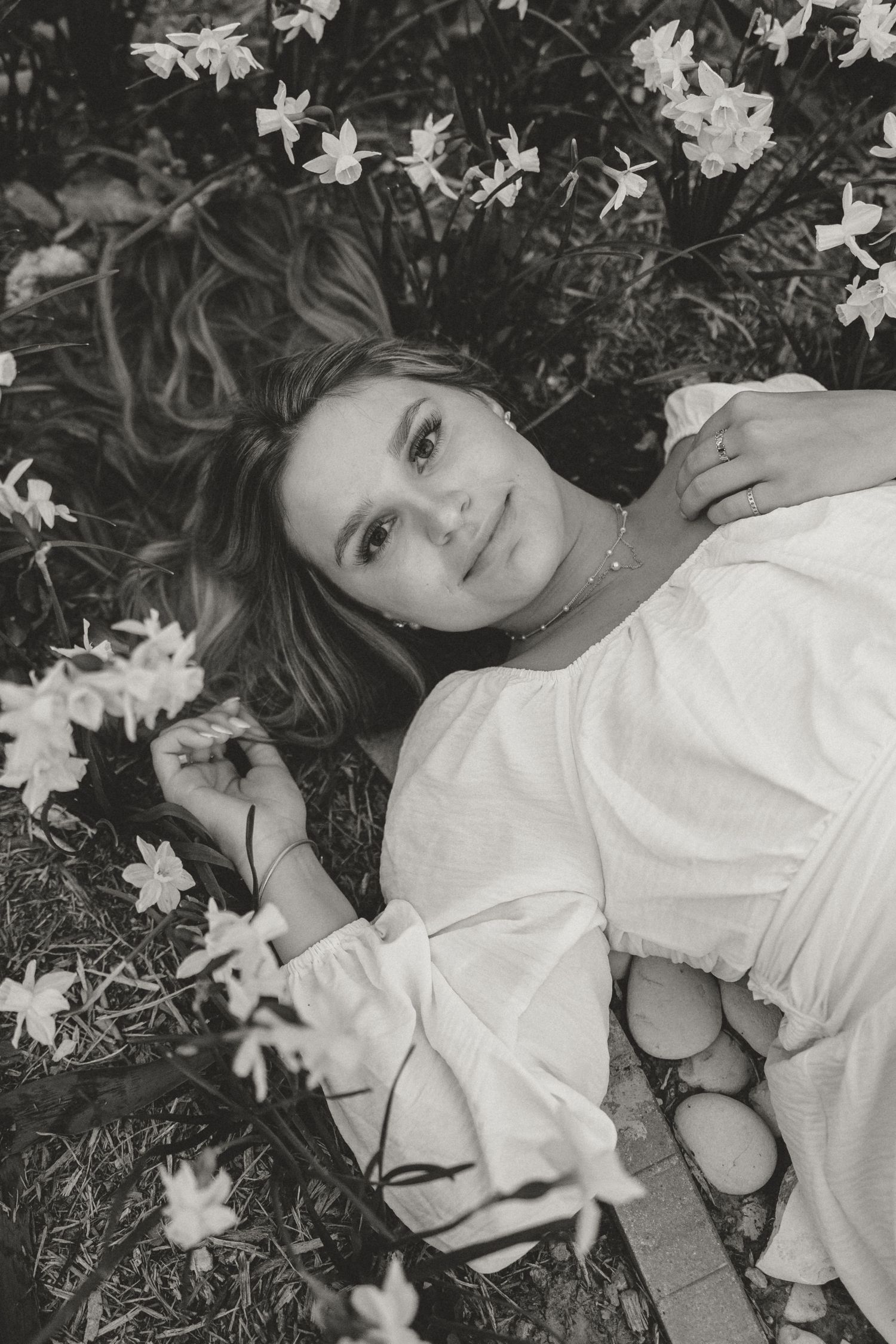 Black and white portrait of person lying in field of white flowers.