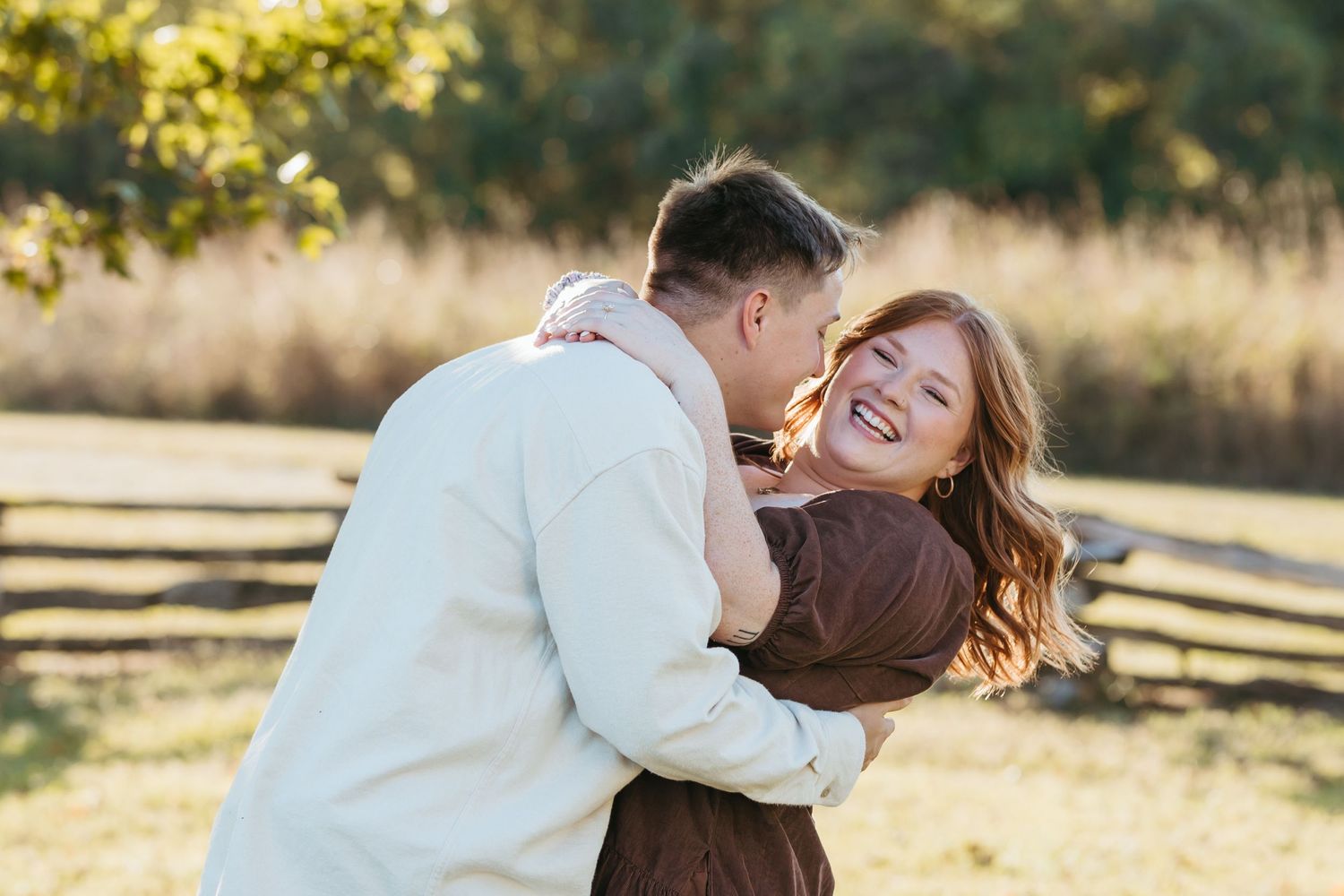 Couple sharing playful moment in golden sunset light near rustic fence.