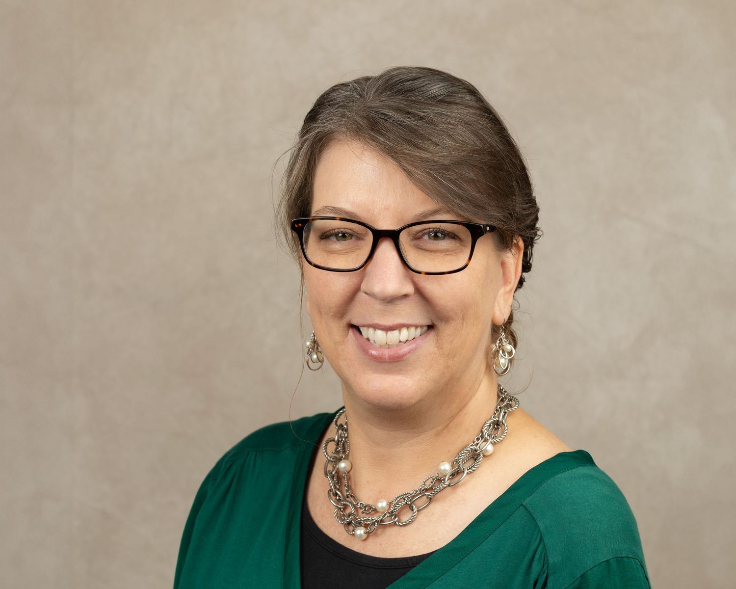 Professional portrait of a person wearing glasses and a green cardigan with statement necklace.