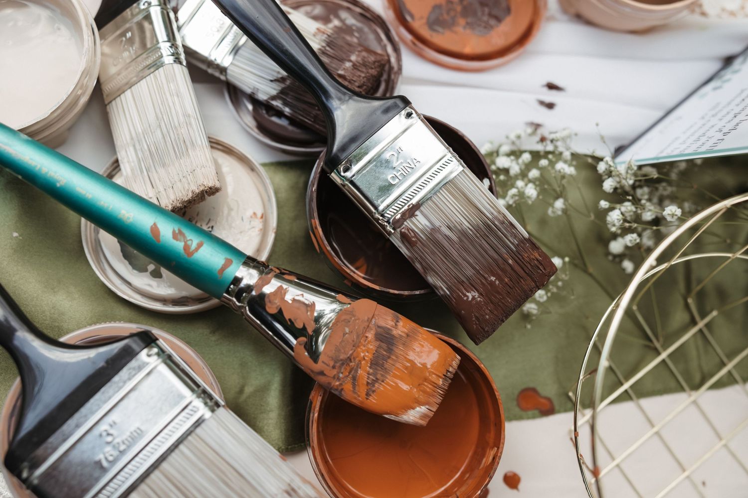 Collection of paint brushes and supplies arranged on a light surface.