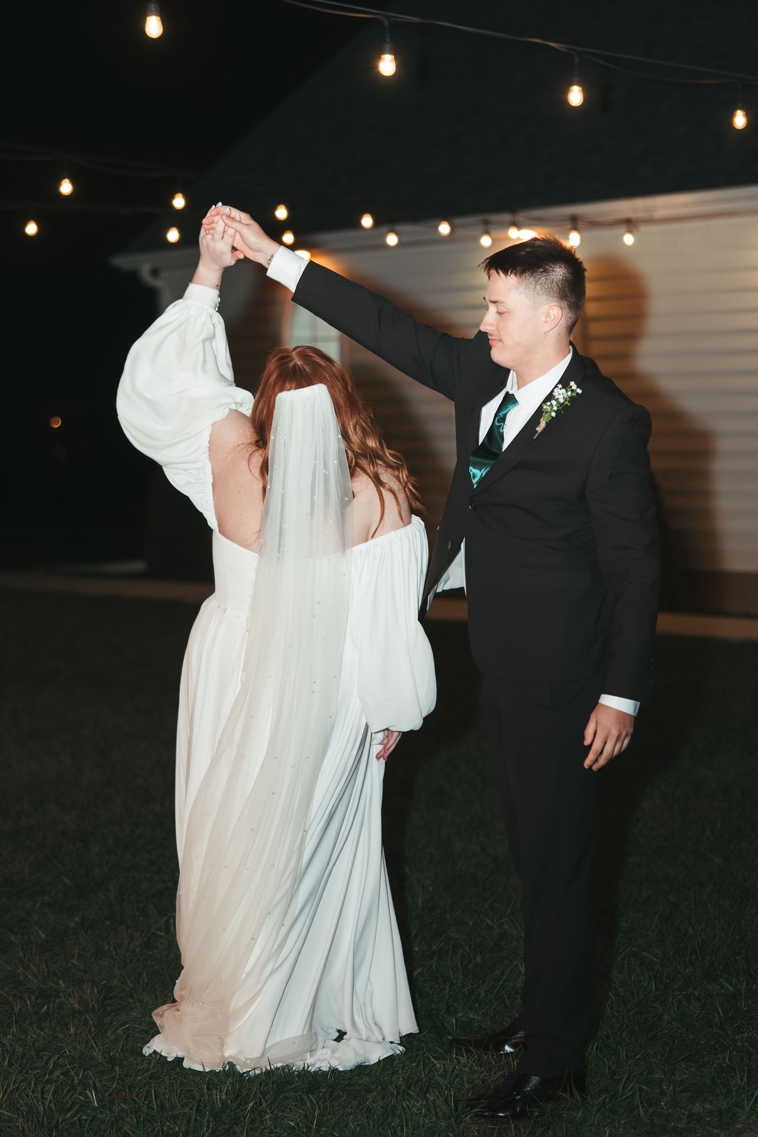 A couple dancing under string lights, with the bride's dress flowing gracefully.