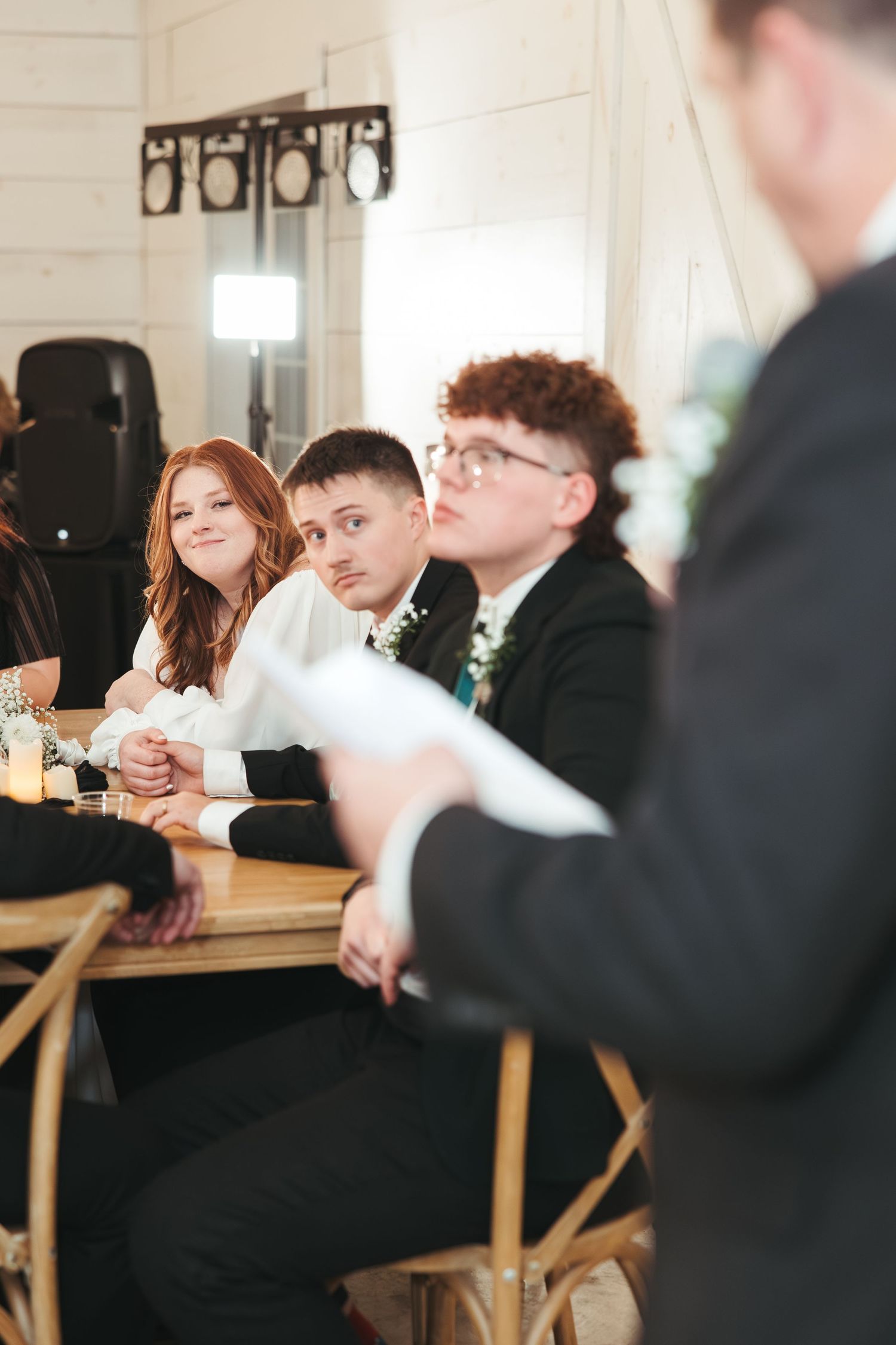 Wedding guests seated at tables during reception event with stage lighting equipment visible in background.