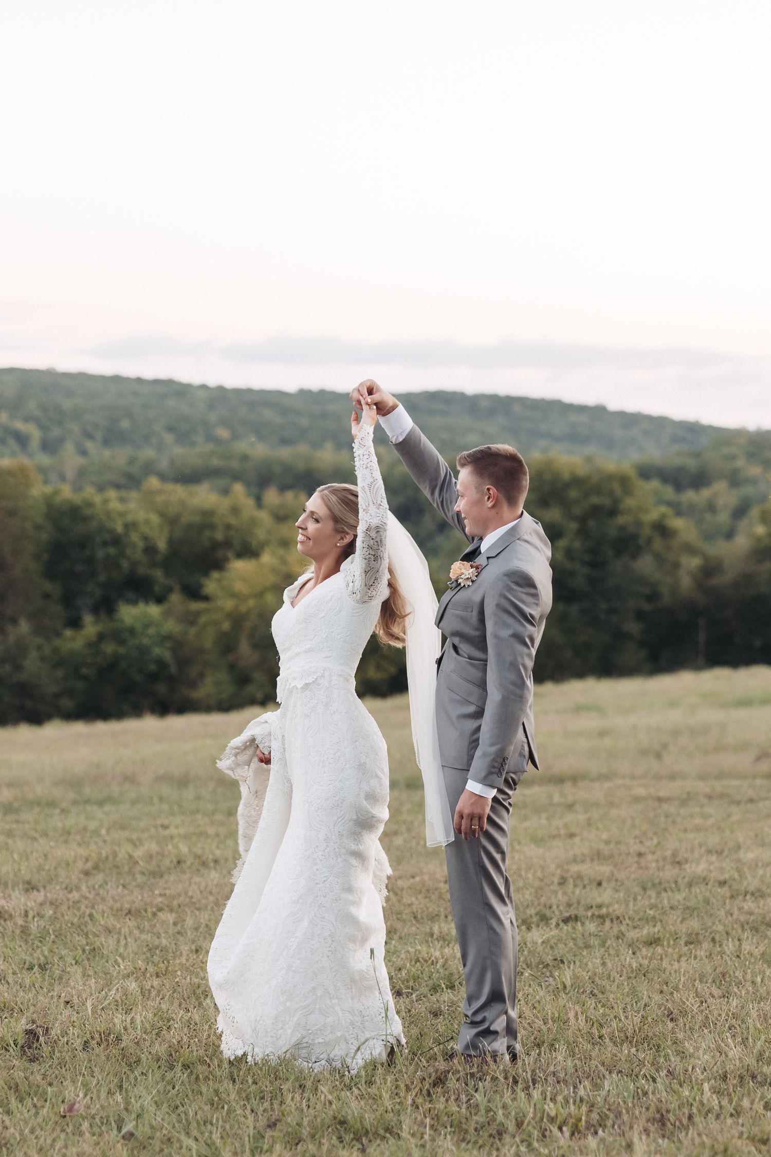 Joyful wedding couple dancing in mountain field during golden hour.