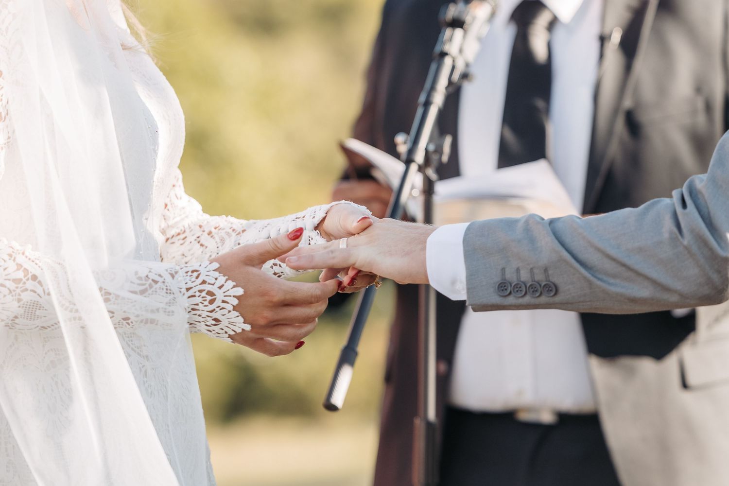 Close up of hands exchanging rings during an outdoor wedding ceremony.