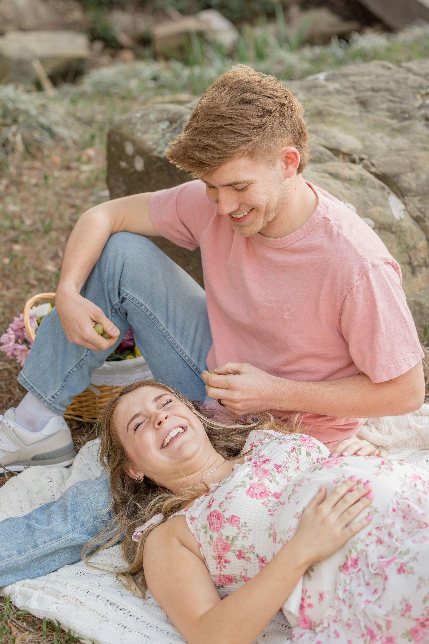 A couple laughs together while relaxing on rocks during an outdoor photoshoot.
