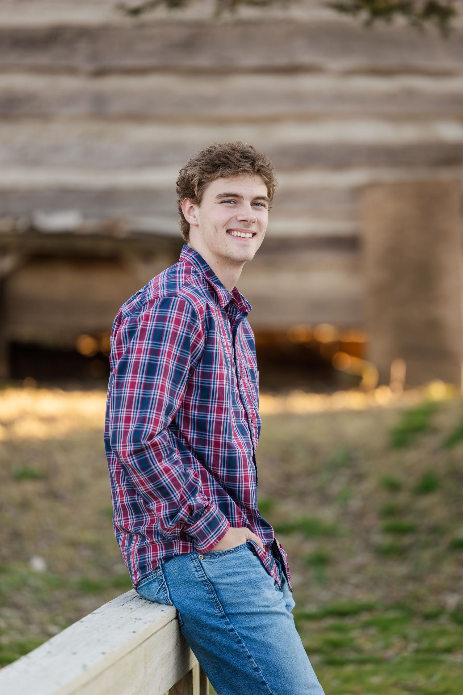 A casual outdoor portrait featuring a plaid button-down shirt and jeans against a rustic wooden background.