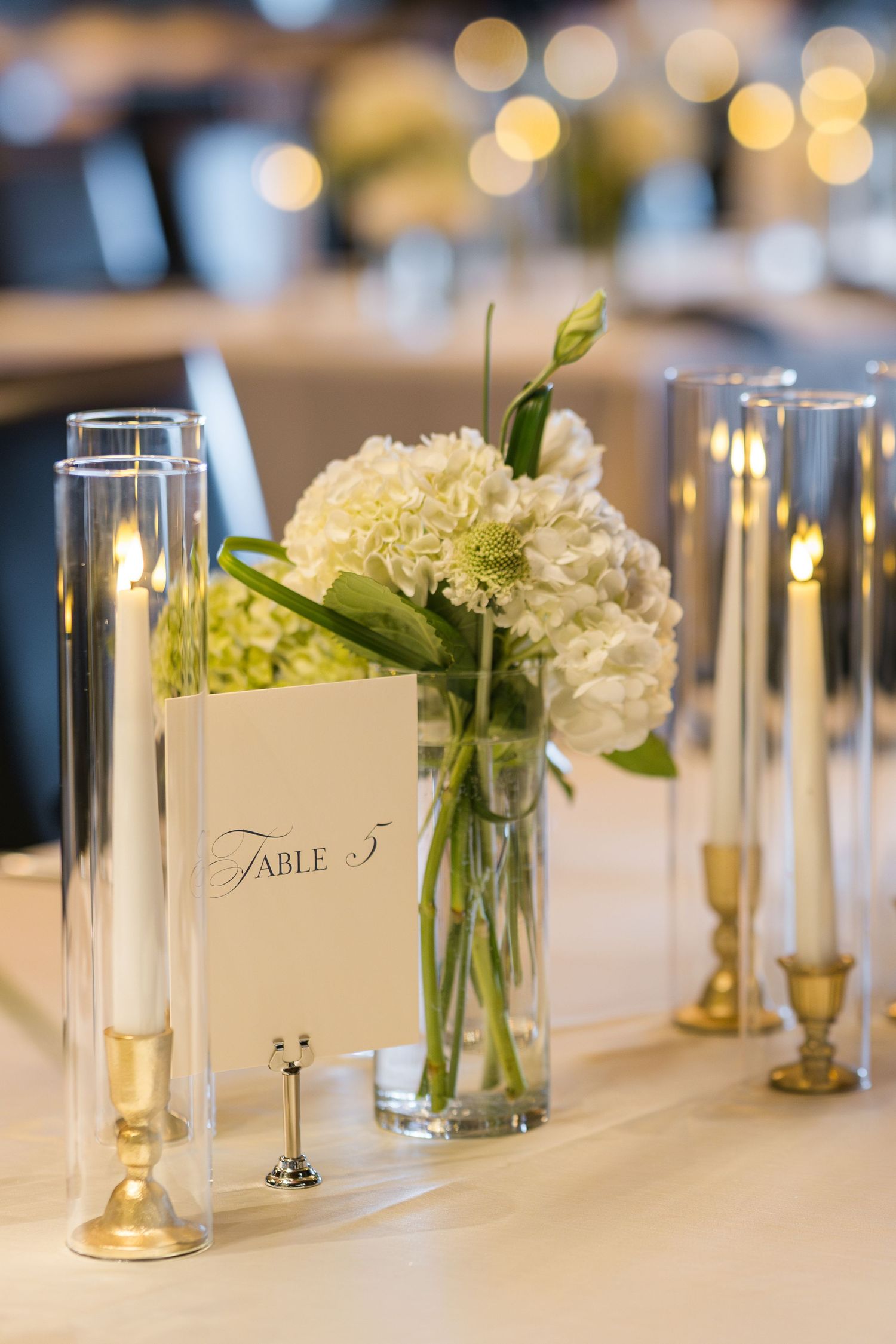 Wedding reception table with white place cards, glass candle holders, and fresh floral centerpieces.