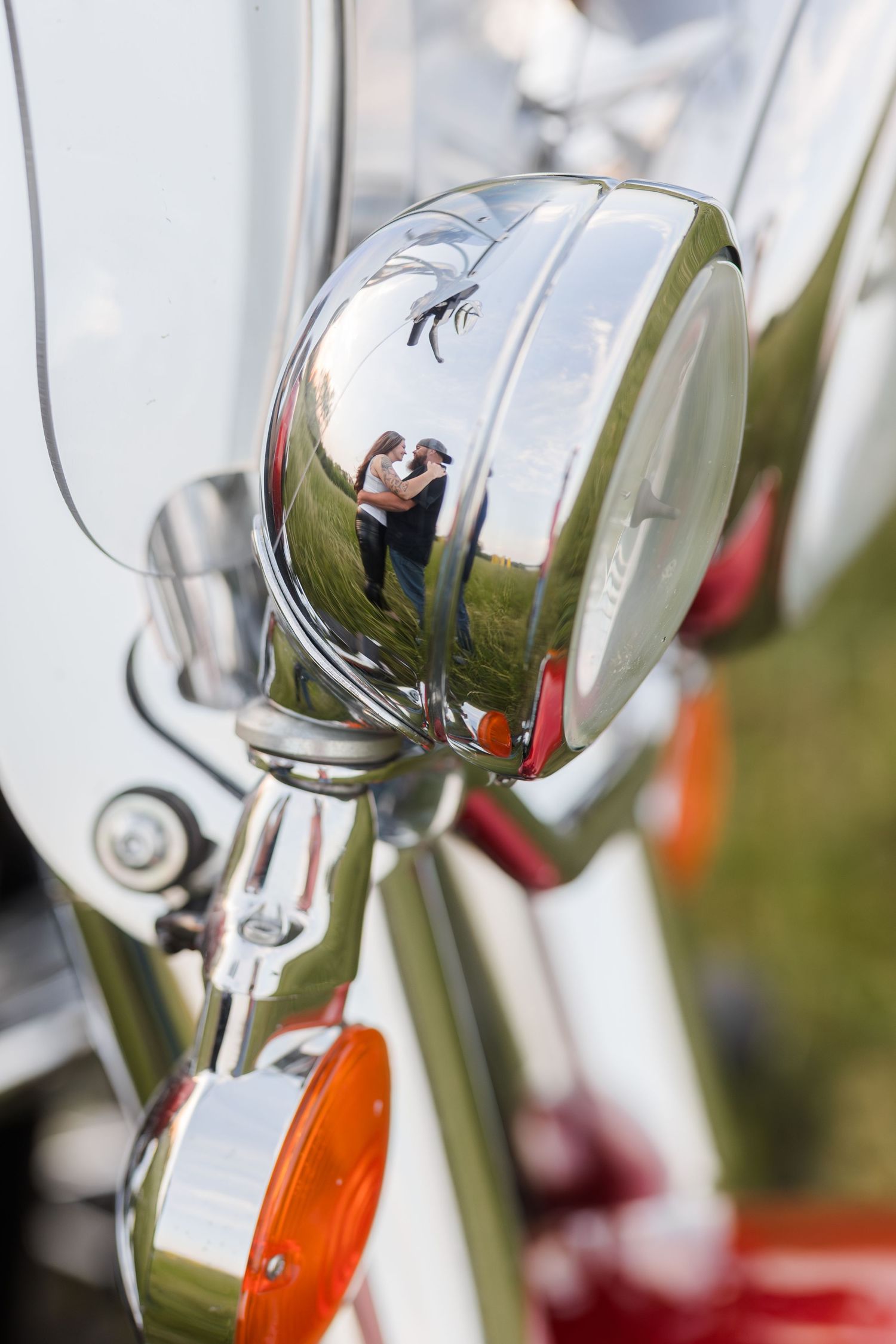 Chrome motorcycle headlight reflects sun and scenery in its polished metallic surface while mounted on bike.