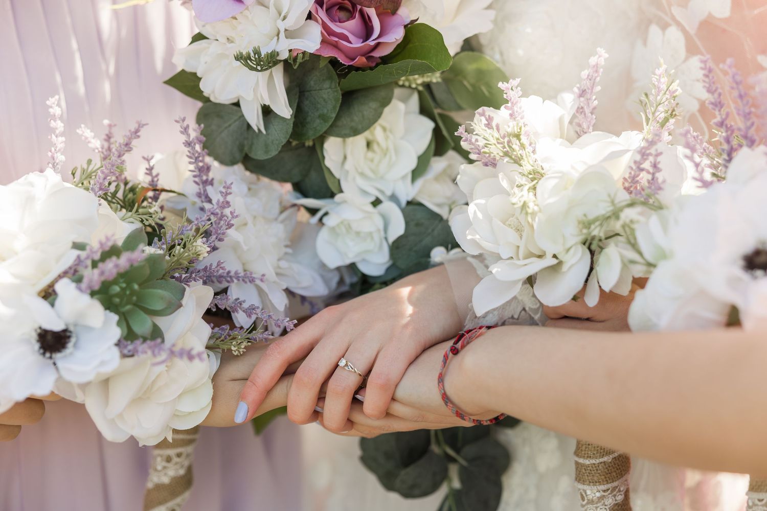 Wedding ring shown against backdrop of elegant white and pink floral arrangements with lush greenery.