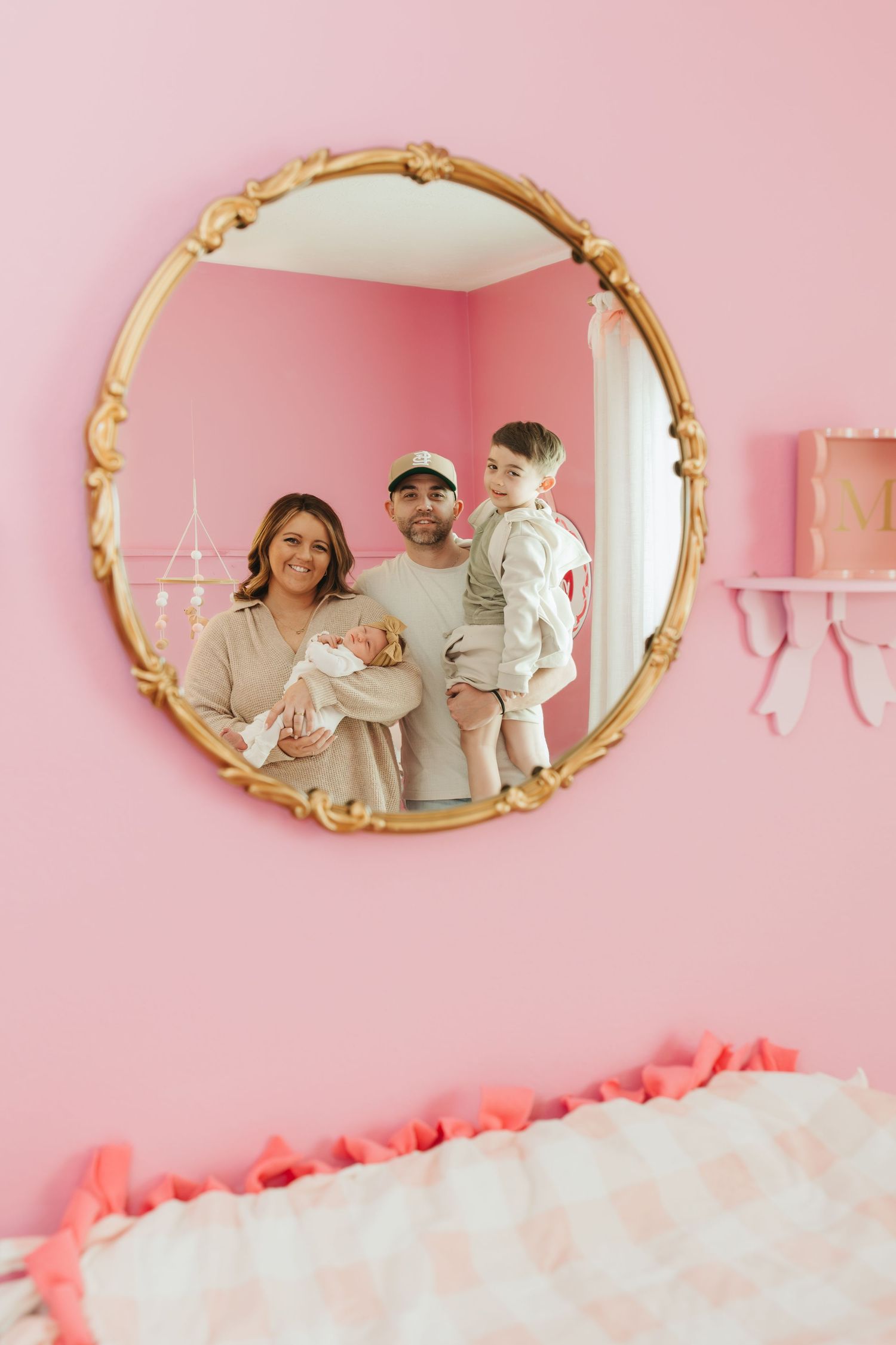 A round gold mirror reflects a family scene against a pink nursery wall with decorative shelving.