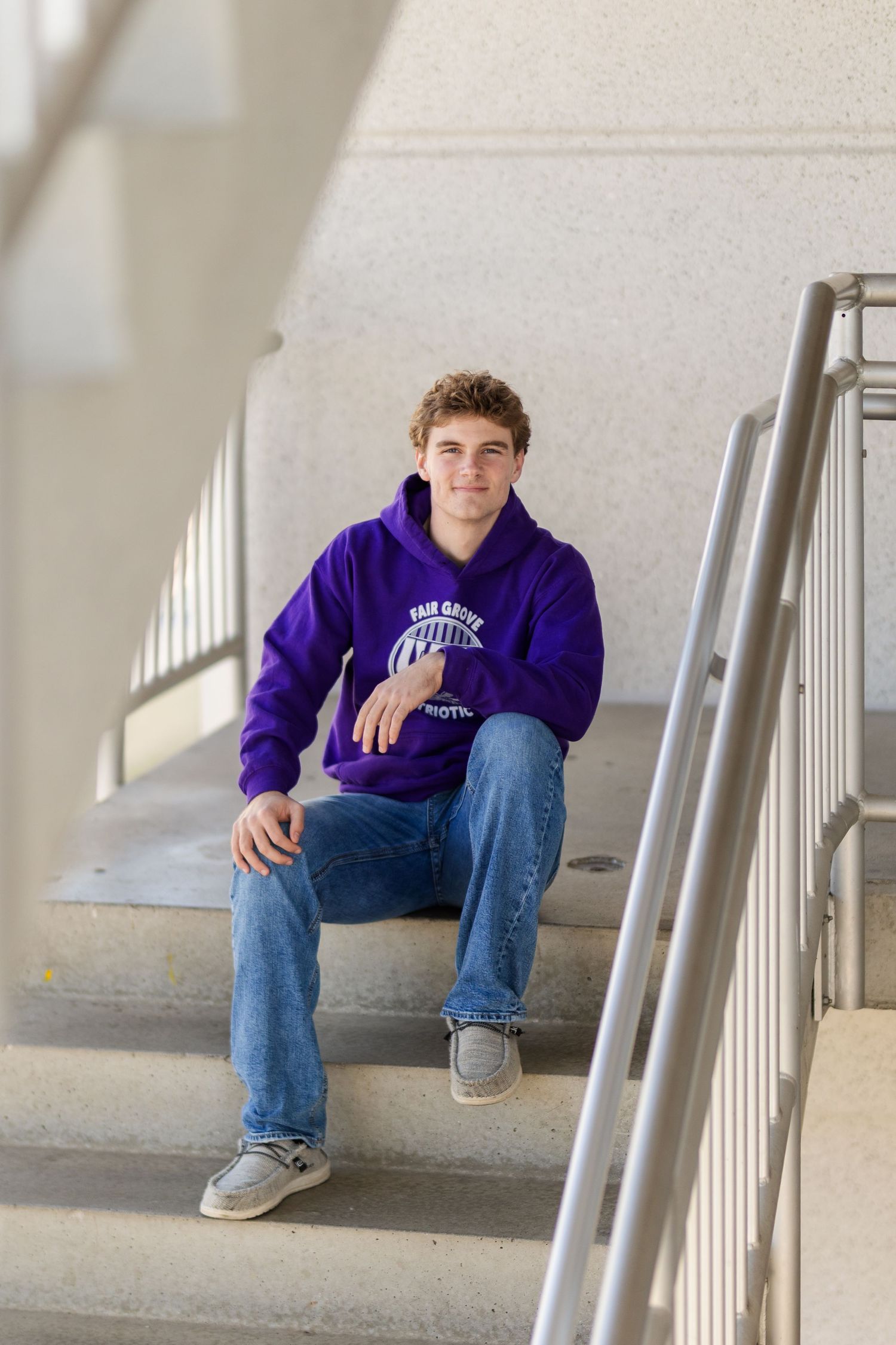 A candid portrait of someone wearing a purple hoodie while sitting on concrete stairs.