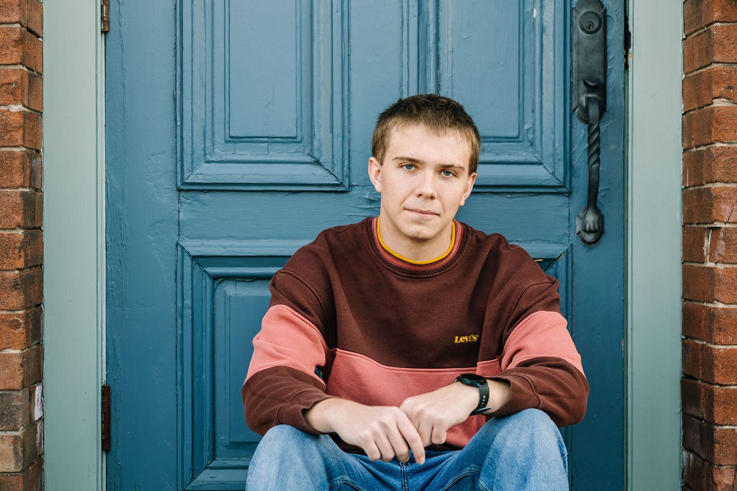 A person in a brown sweater sits on stone steps in front of a bright turquoise blue door.