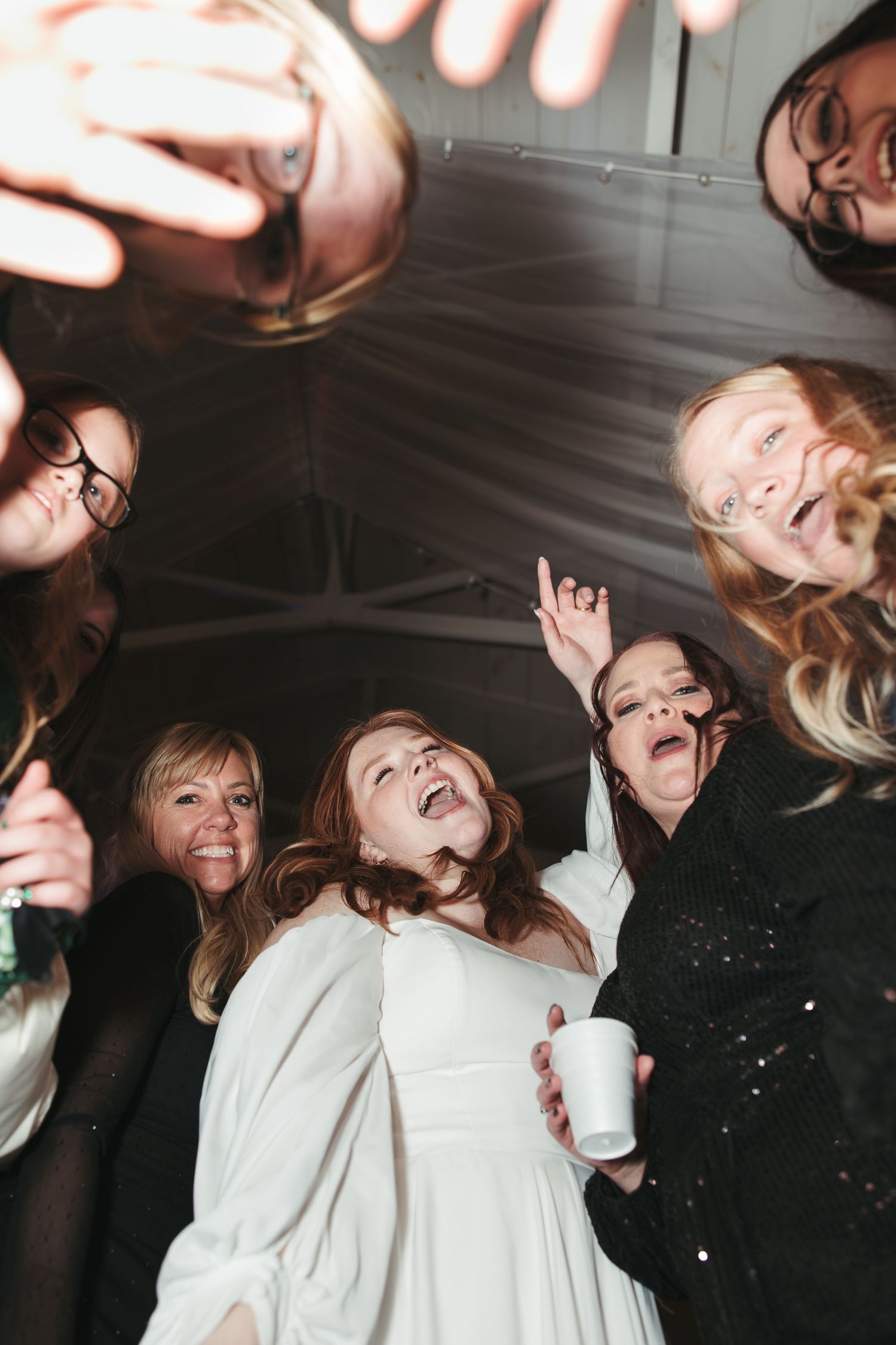 Circular group photo from below showing wedding party laughing and celebrating with drinks.
