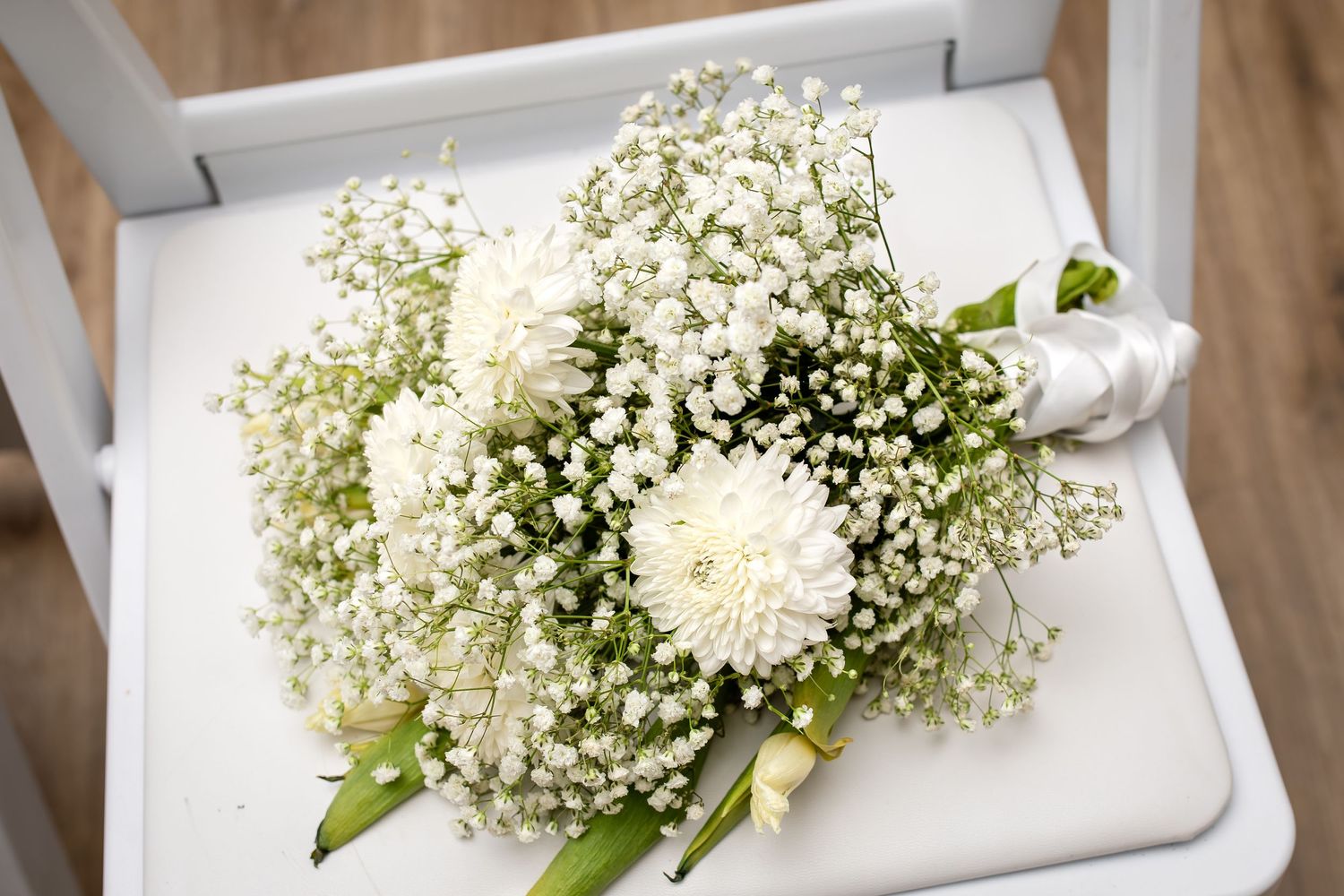 A delicate white wedding bouquet featuring baby's breath and chrysanthemums on a light surface.