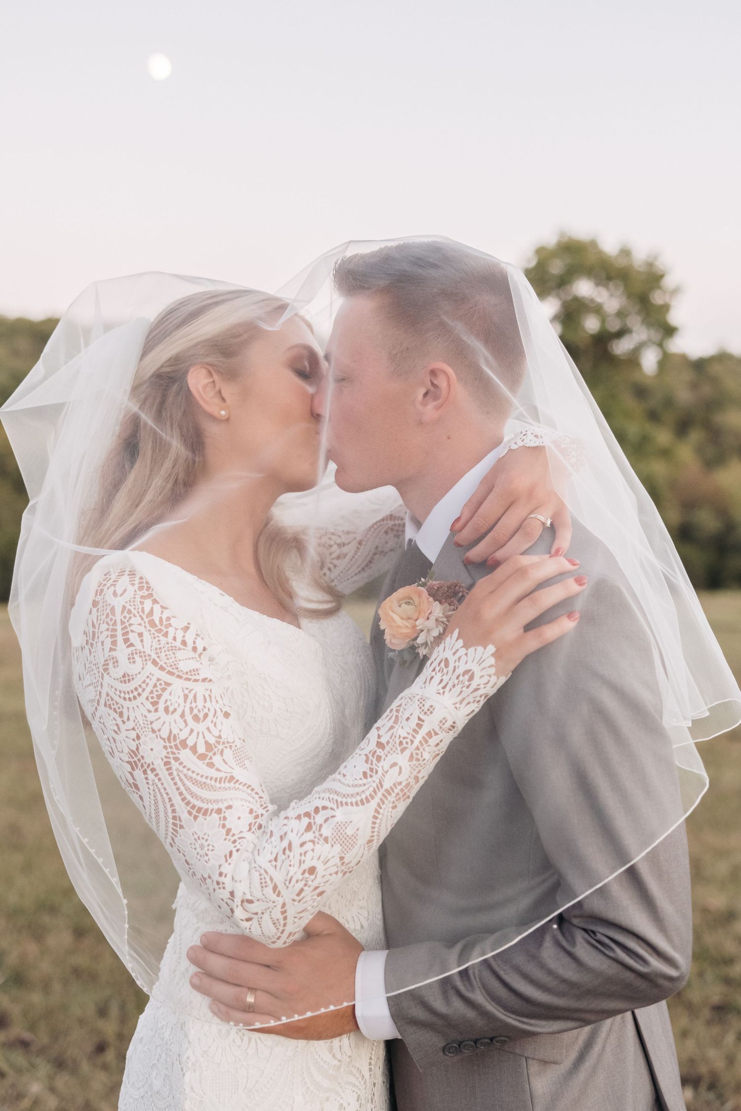 Romantic wedding portrait captured under a flowing veil as couple shares intimate moment.