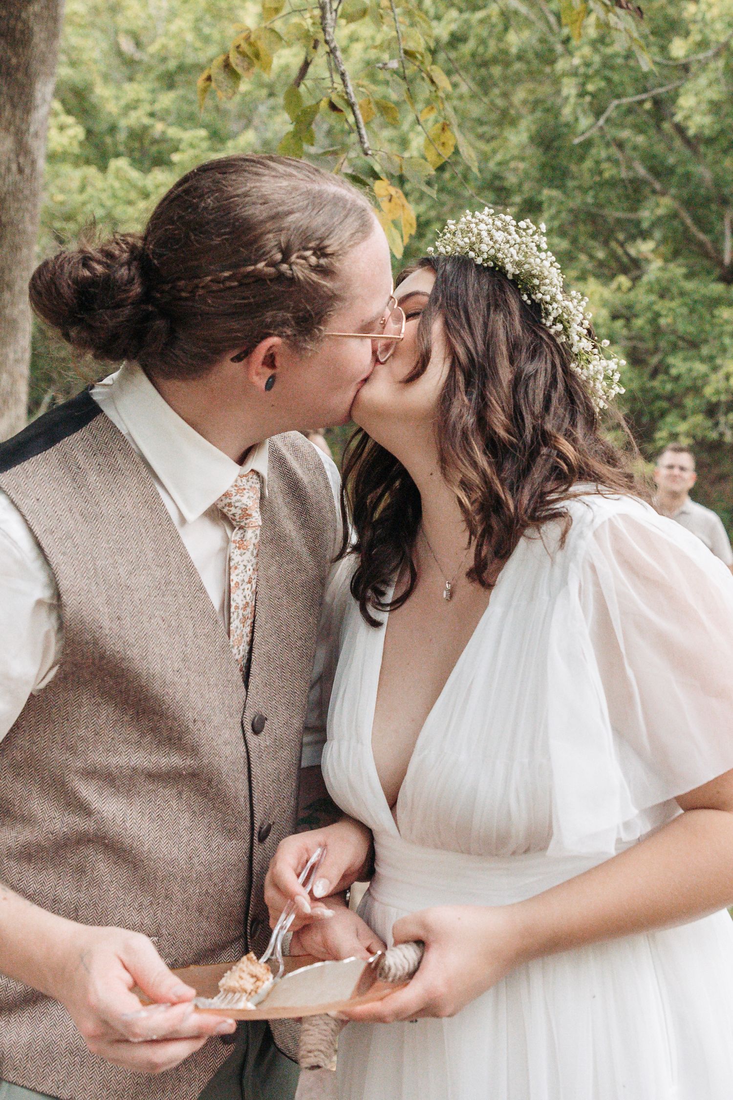 A romantic wedding moment showing a couple sharing a kiss while holding white floral decorations.
