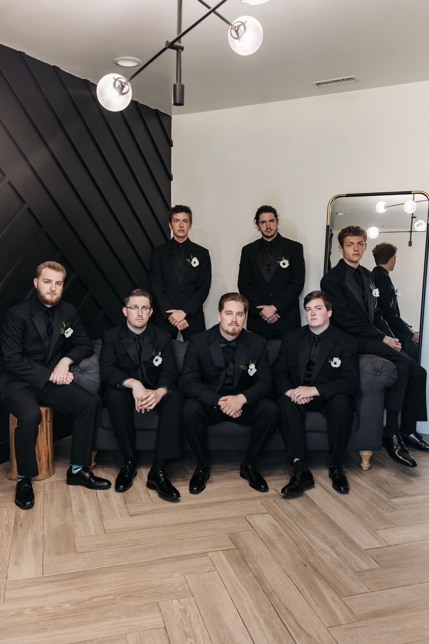 Groomsmen in matching black suits posed for formal group photo on herringbone floor.