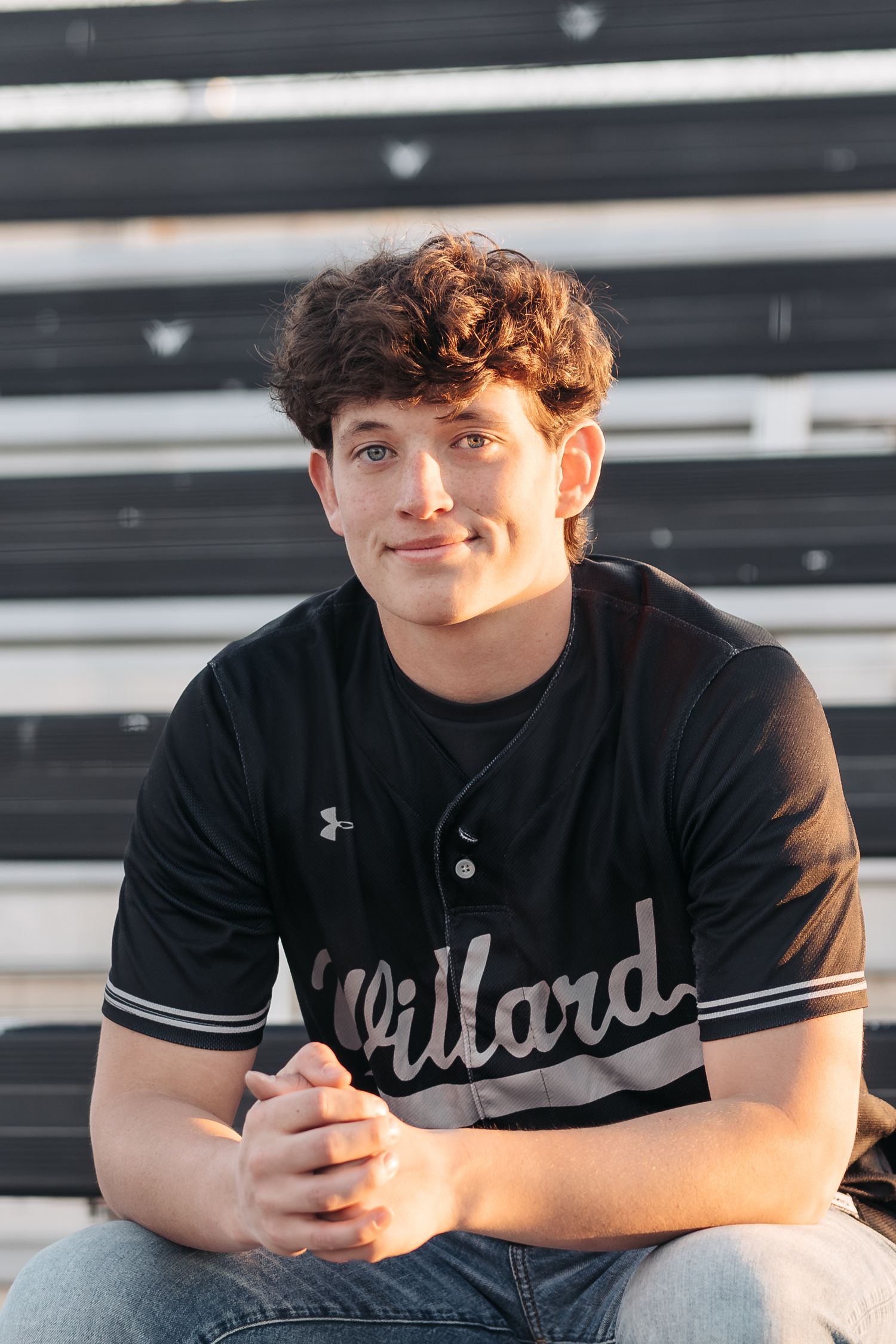 Baseball player wearing Willard jersey sitting on bleachers during portrait session.