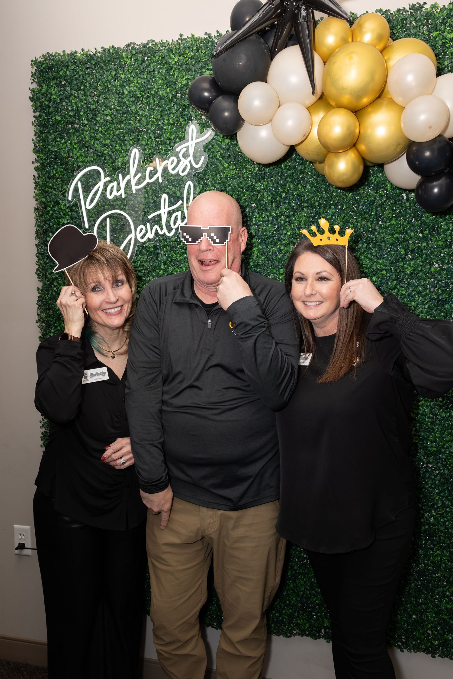 Dental office party photo with balloon arch and green backdrop featuring staff in black attire.