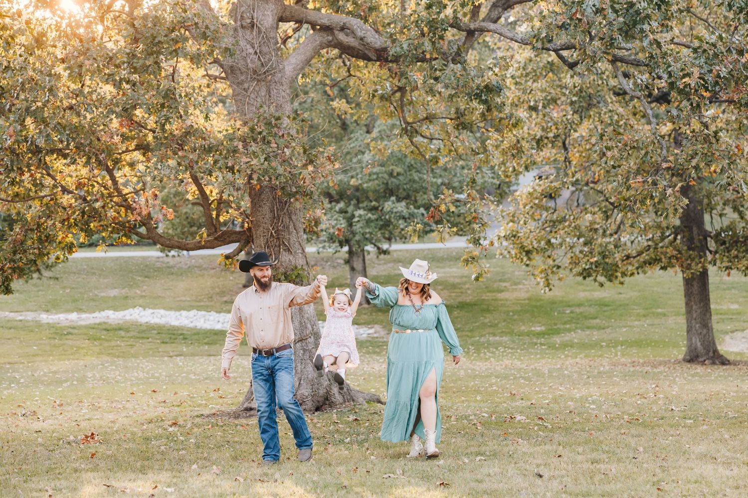 A joyful family plays together in a sunlit park with autumn trees in the background.
