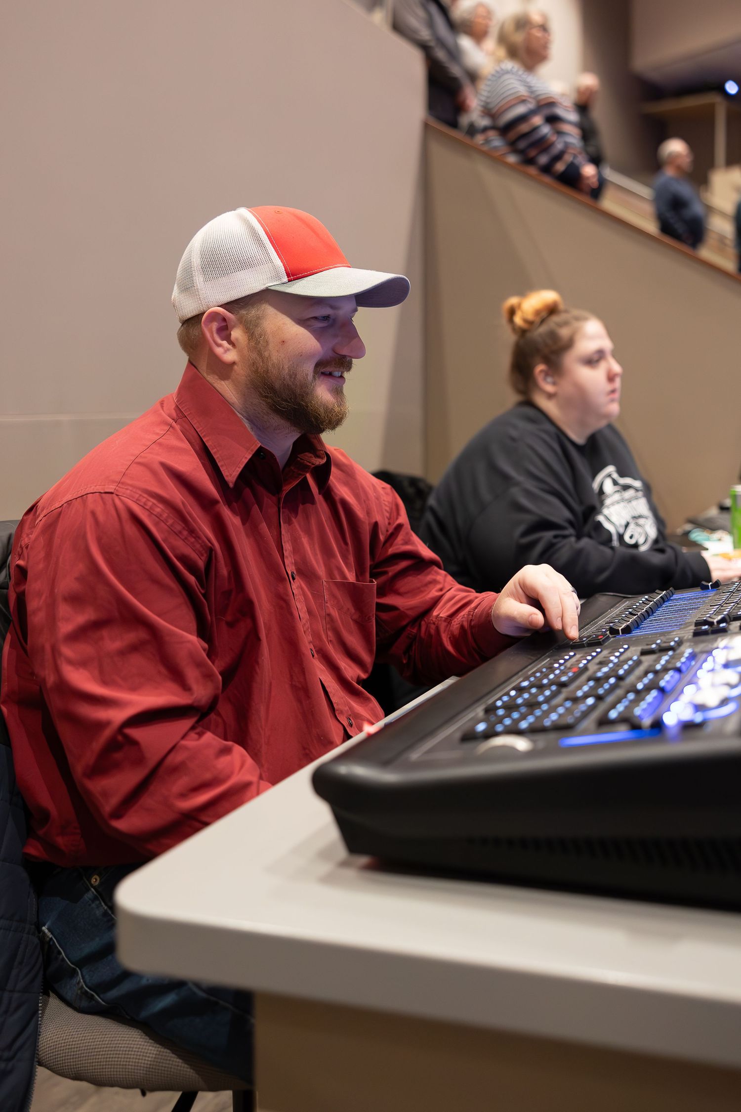 Audio technician in red shirt and baseball cap operating sound equipment.