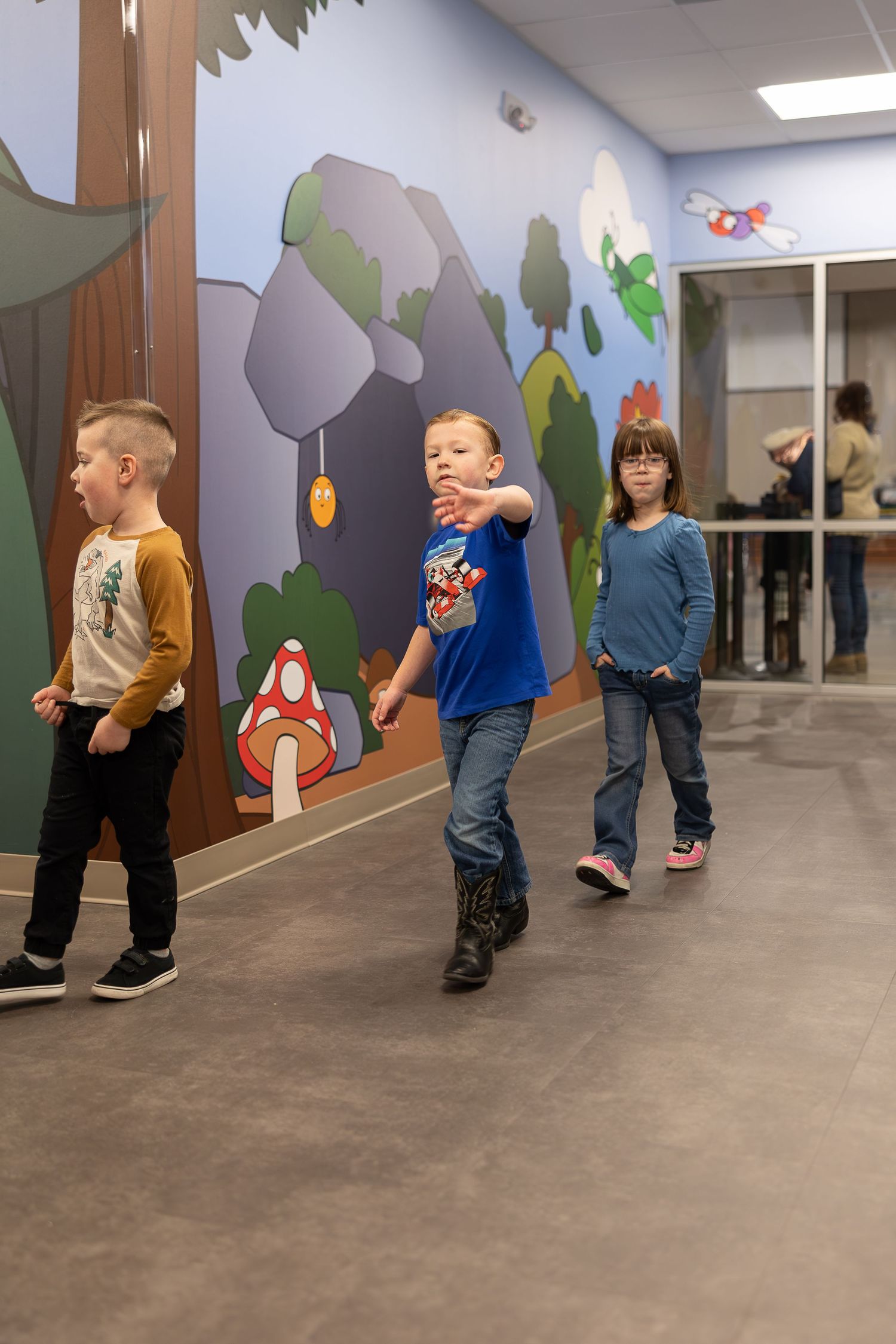 Students walk in line along a hallway decorated with whimsical forest-themed wall art.