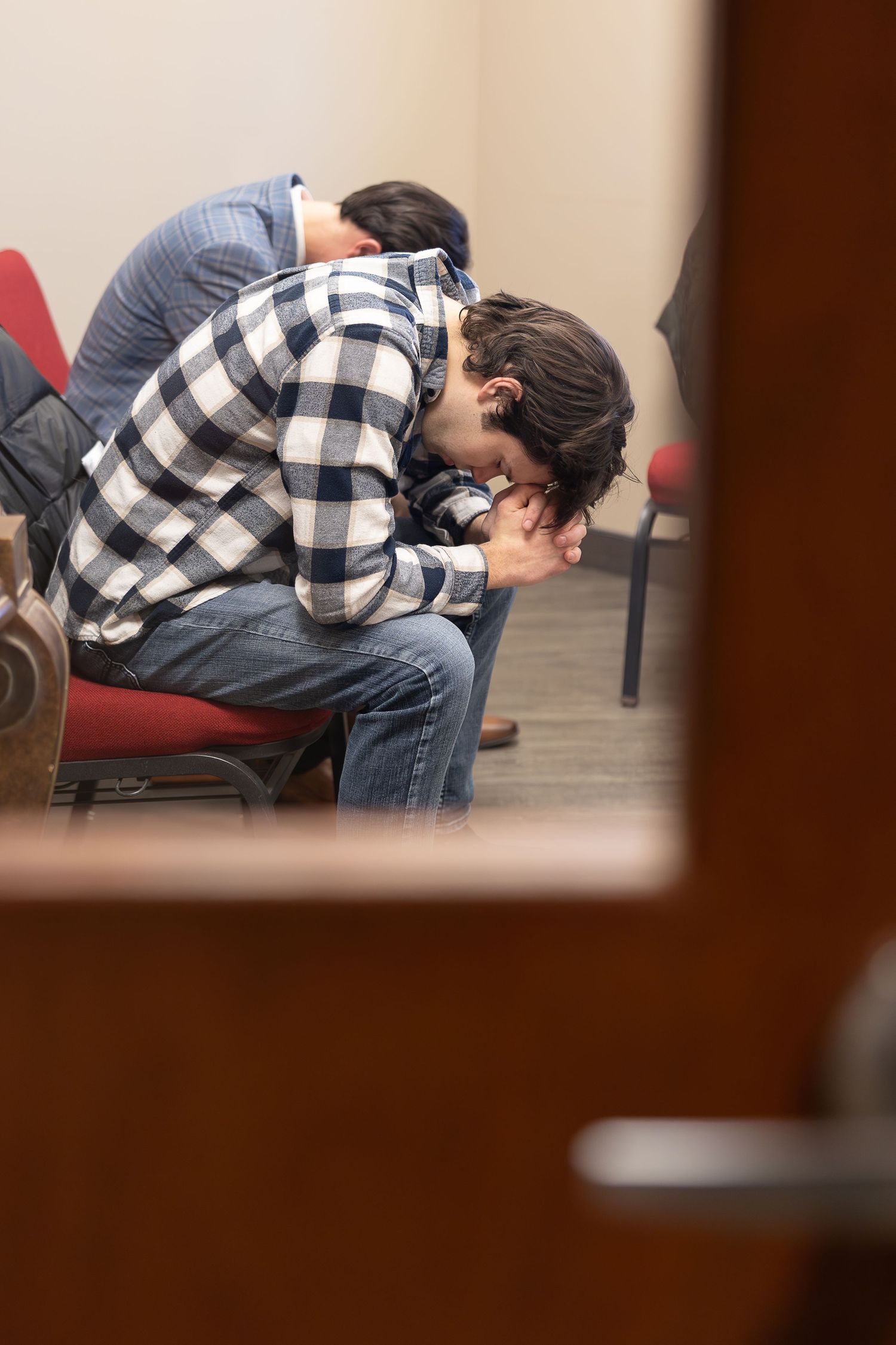Person sits hunched over in chair in casual plaid shirt.