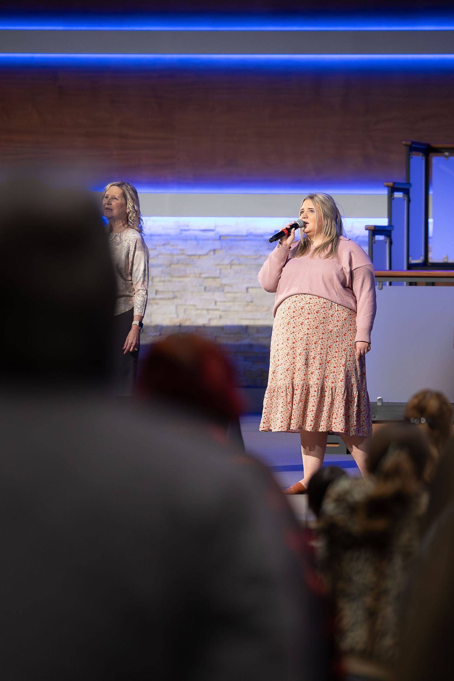 Two performers singing on stage during a church service with blue lighting.