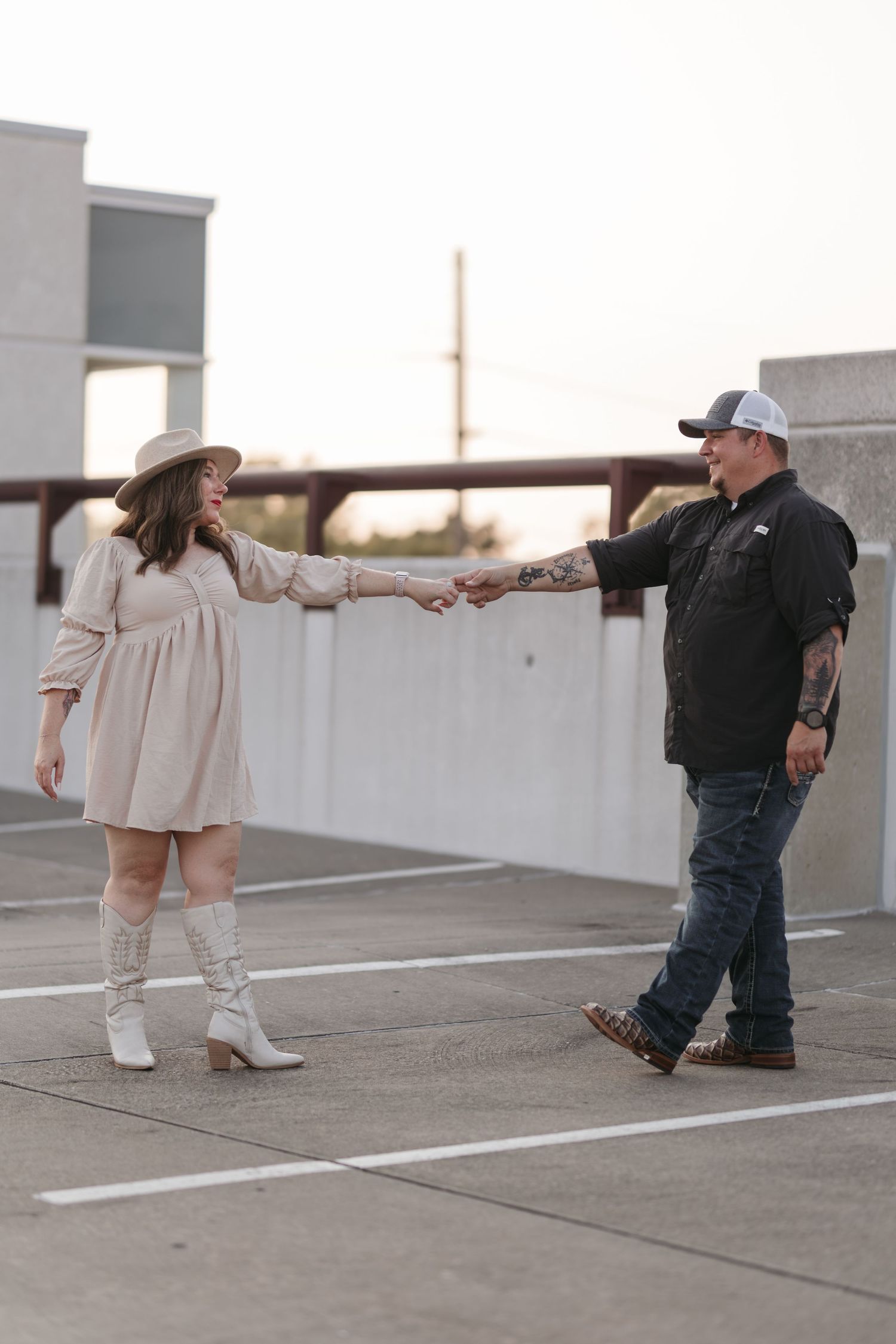 A couple in contrasting outfits holding hands on a rooftop parking area.