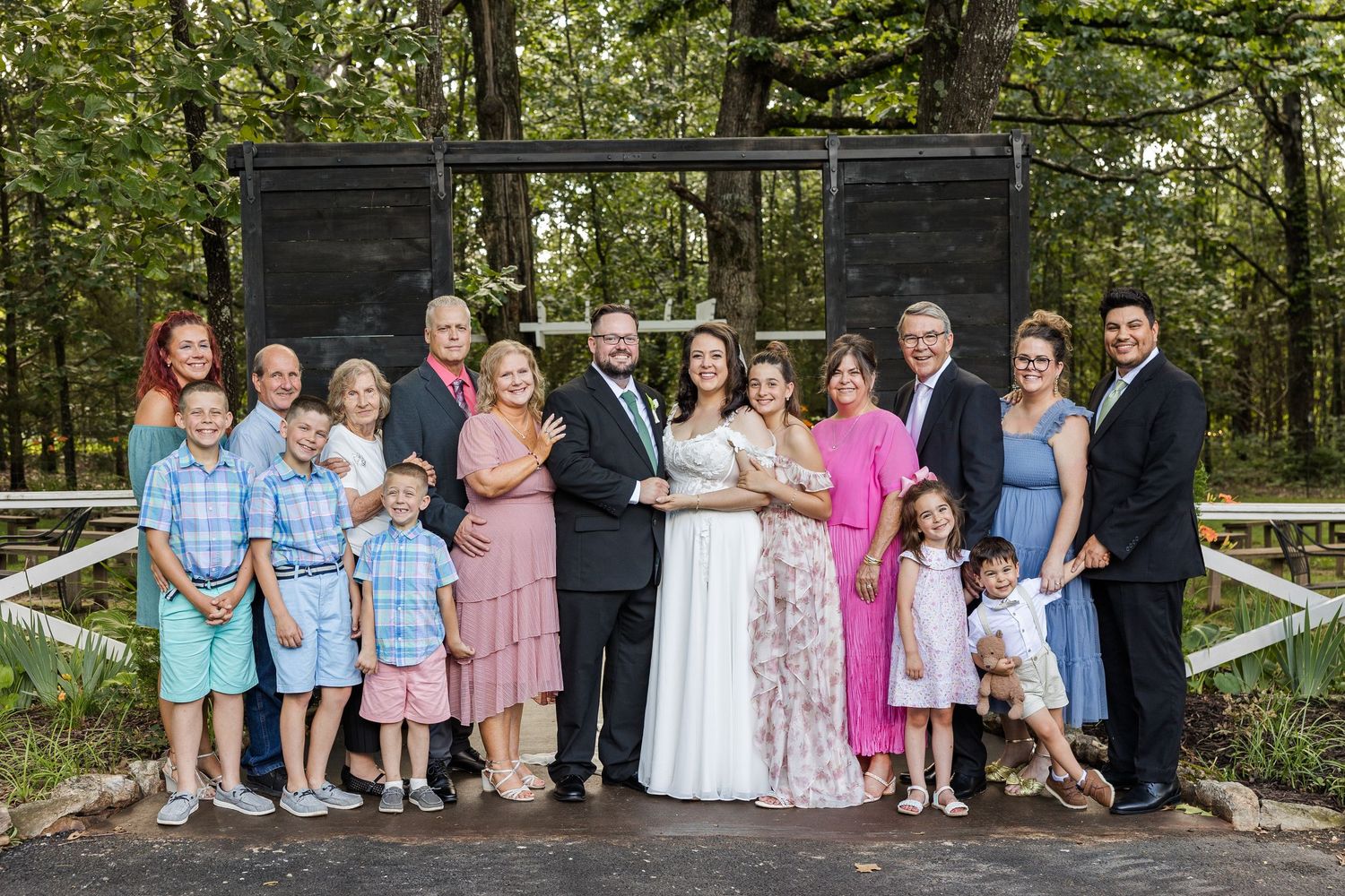Family group stands together on a wooden bridge surrounded by lush green forest in summertime outdoor setting.