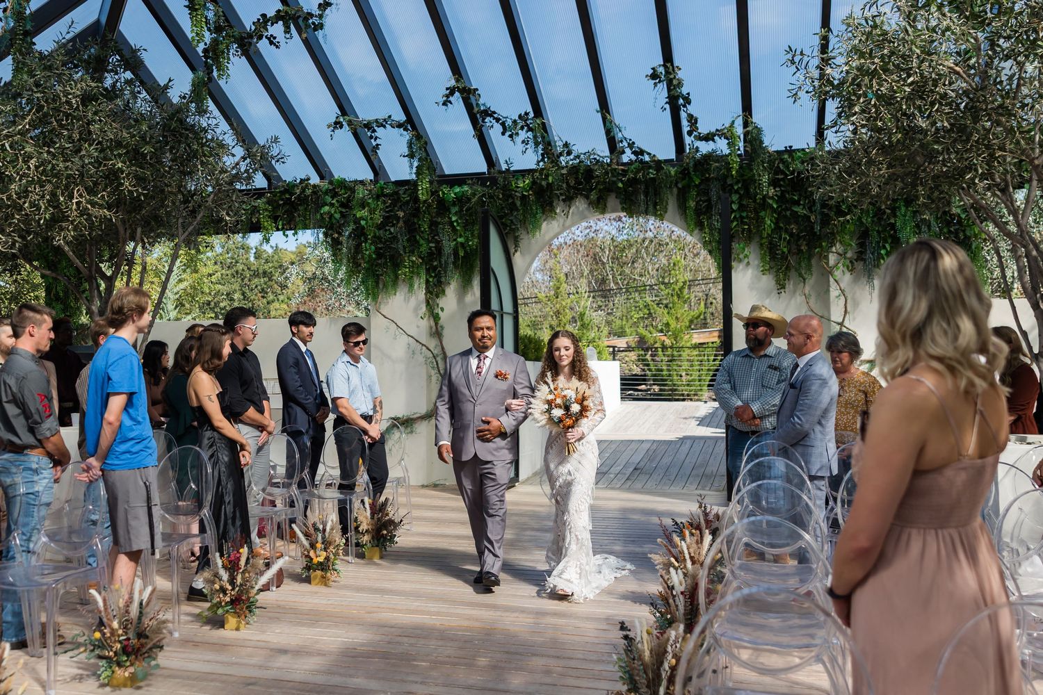 Bride and groom walk down the aisle together in a stunning greenhouse wedding ceremony with lush greenery.