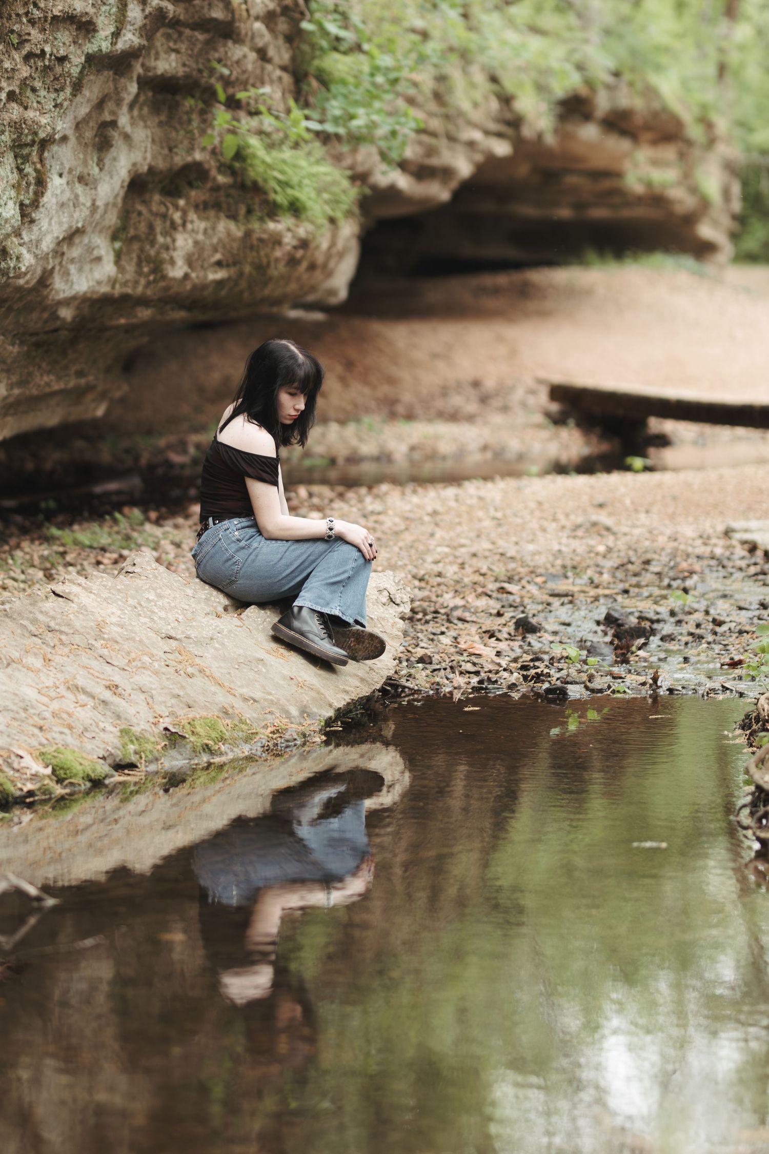 Peaceful scene at a rocky outcrop with a reflection in still water by a cave entrance.