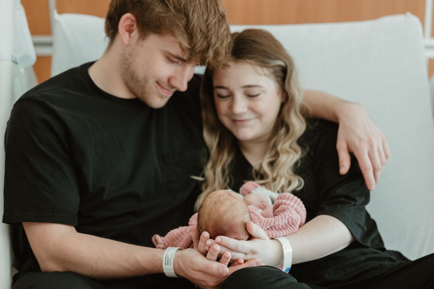 A couple lovingly cuddles their newborn baby while sitting together on a couch.