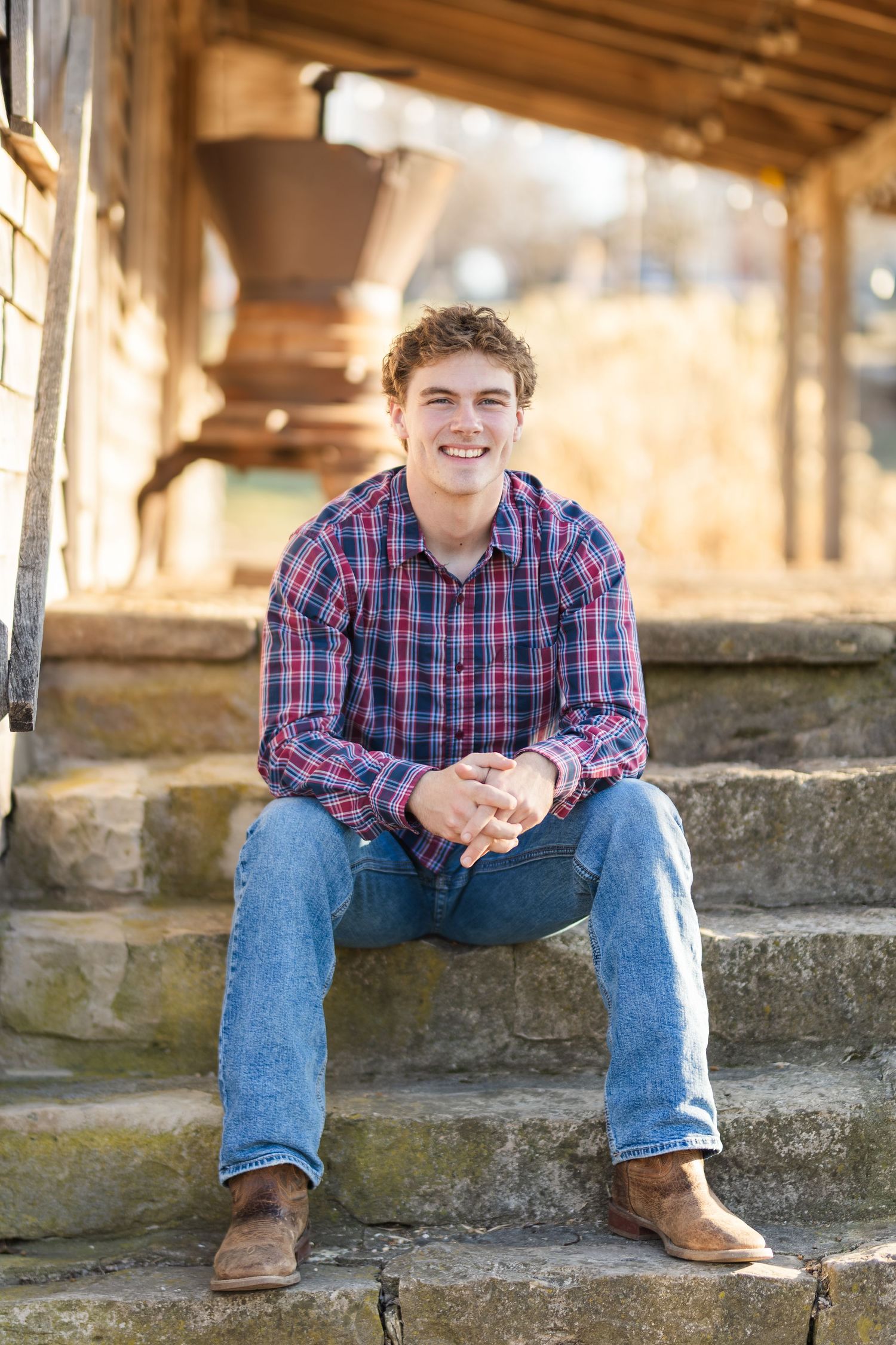 Someone in a plaid shirt and jeans sits casually on outdoor stone steps on a sunny autumn day.