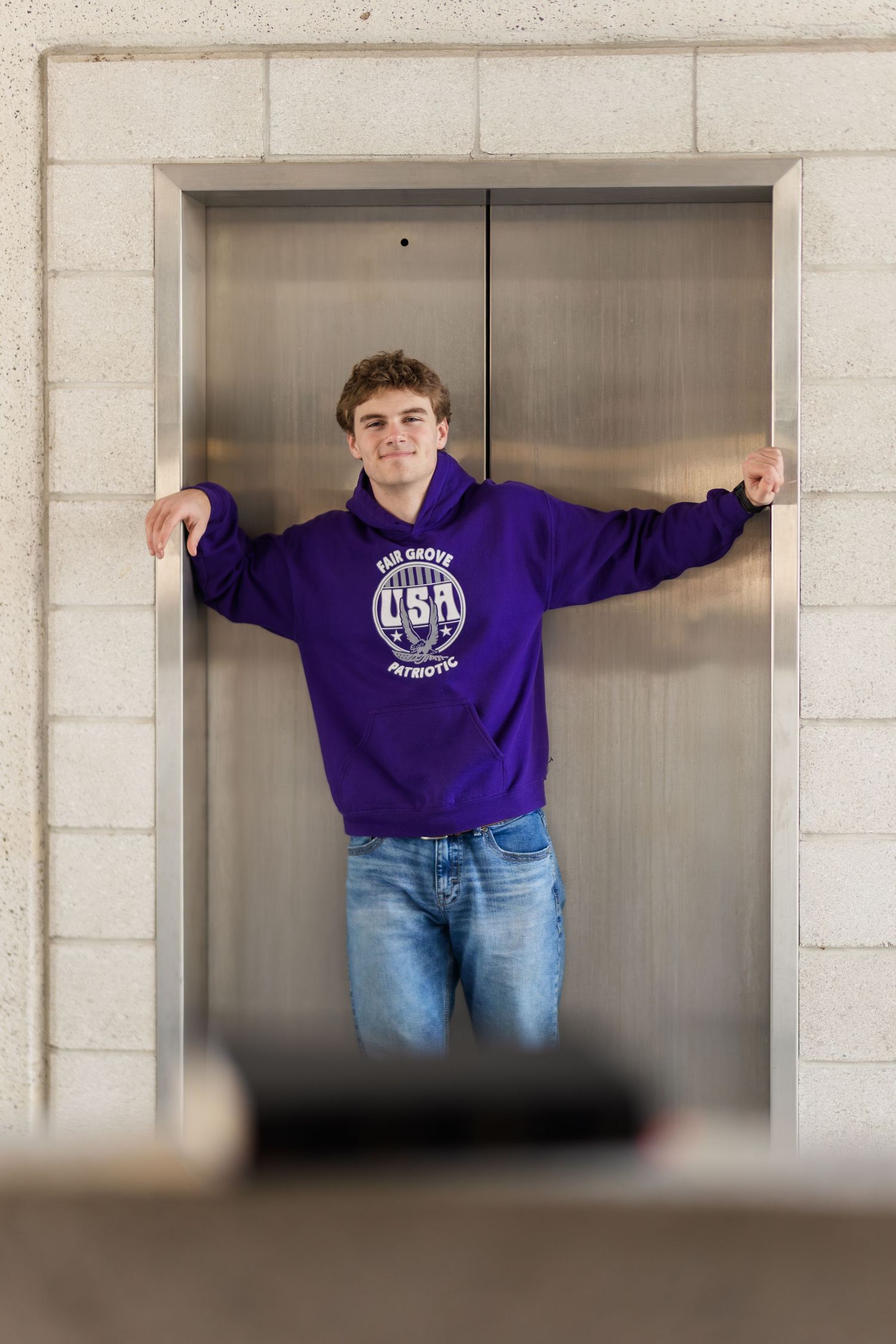 Student in purple hoodie standing by elevator doors in campus building.