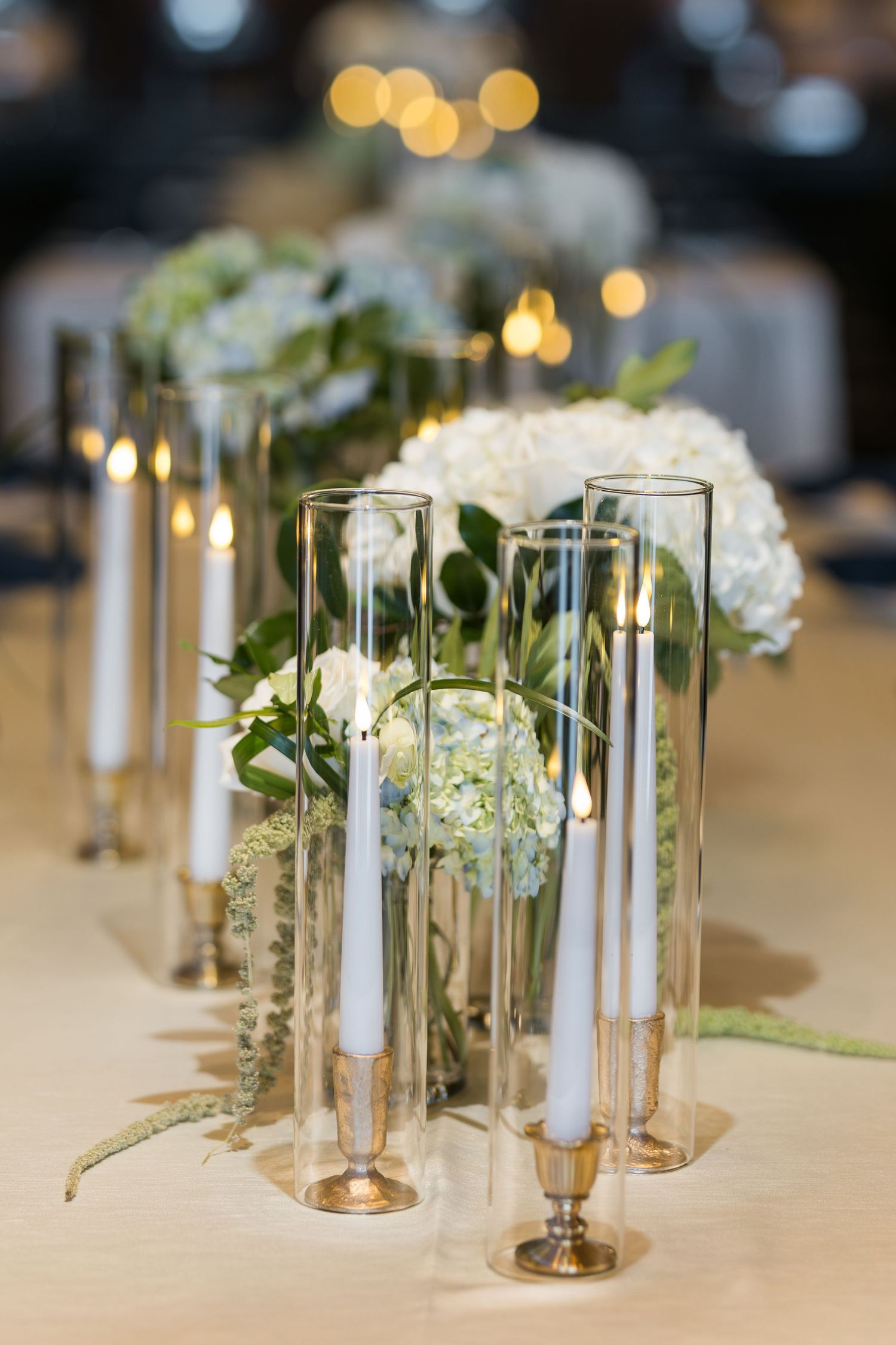 Glass hurricane vases with candles and white floral arrangements create an elegant tablescape.