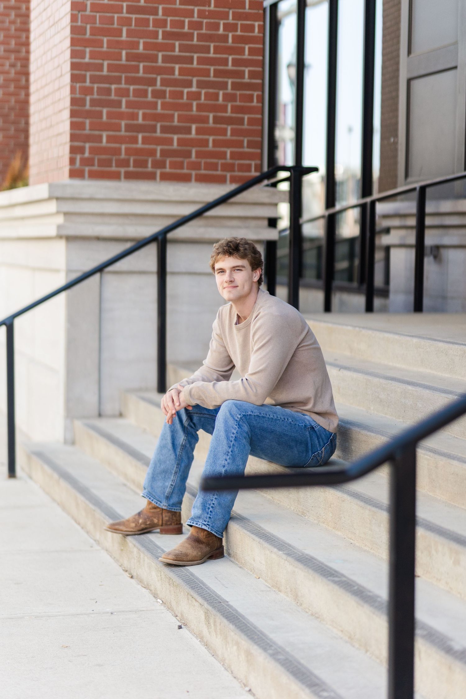 Young person in casual attire sitting on concrete steps outside a brick building.