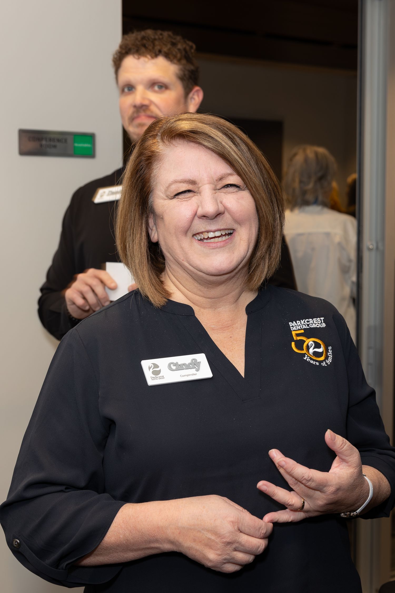 Staff member wearing a navy uniform with a logo smiling during a business event.
