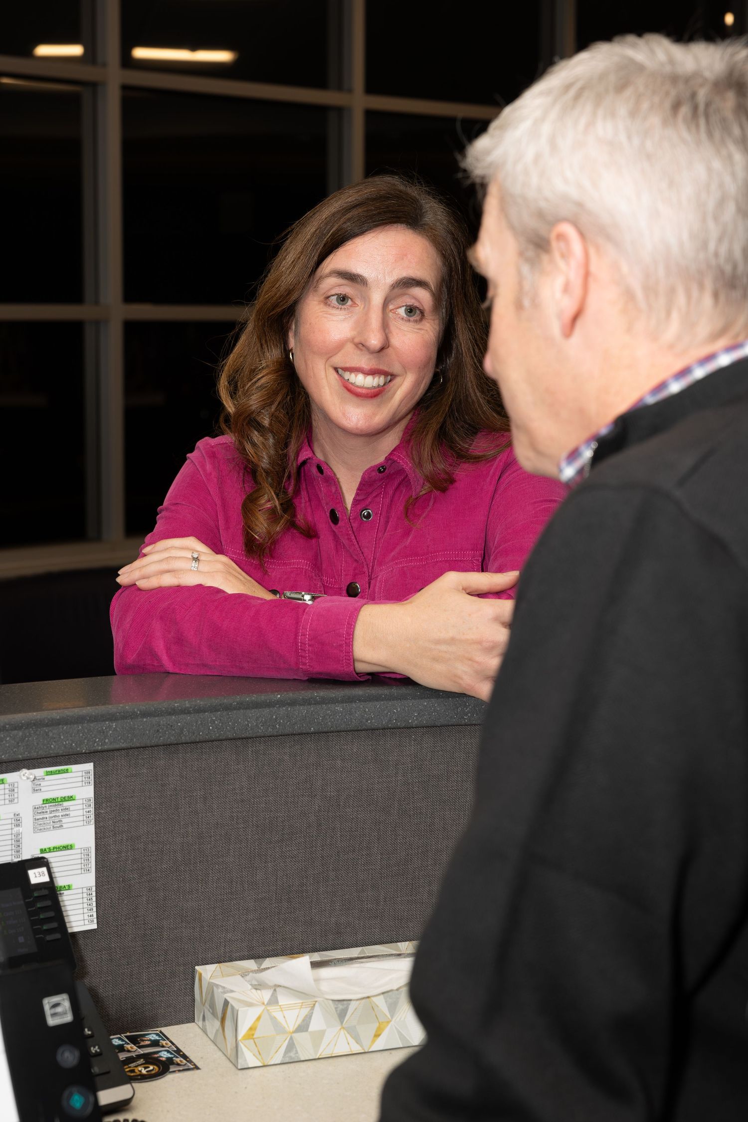 Woman in bright pink top engaged in friendly conversation at office counter.